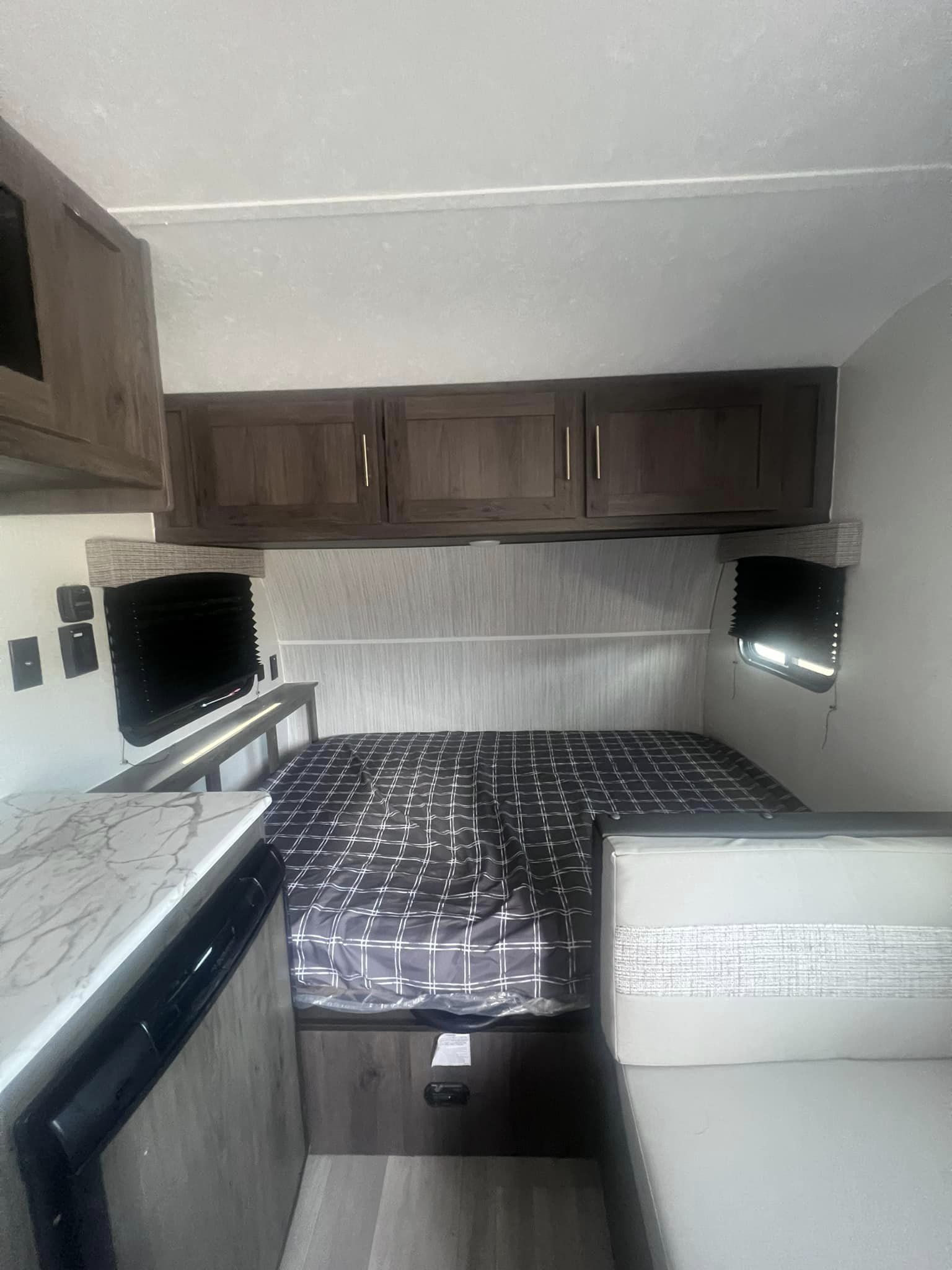 Inside an RV rental, a compact bedroom features a plaid bed, overhead wood cabinets, and a small dining nook, offering a cozy travel living space.. Forest River Viking 2022