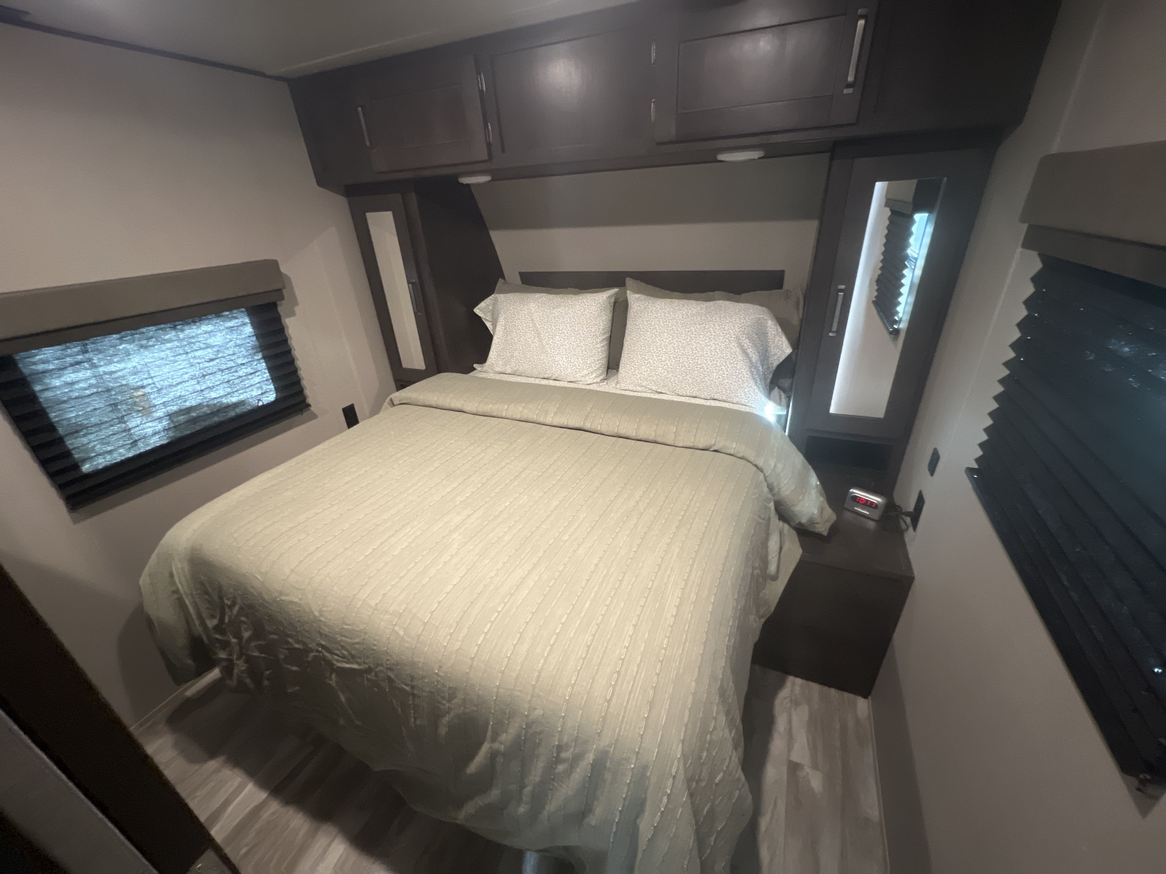 Cozy RV rental bedroom featuring a comfortable bed, dark overhead storage, and window blinds.. Grand Design Transcend 2021