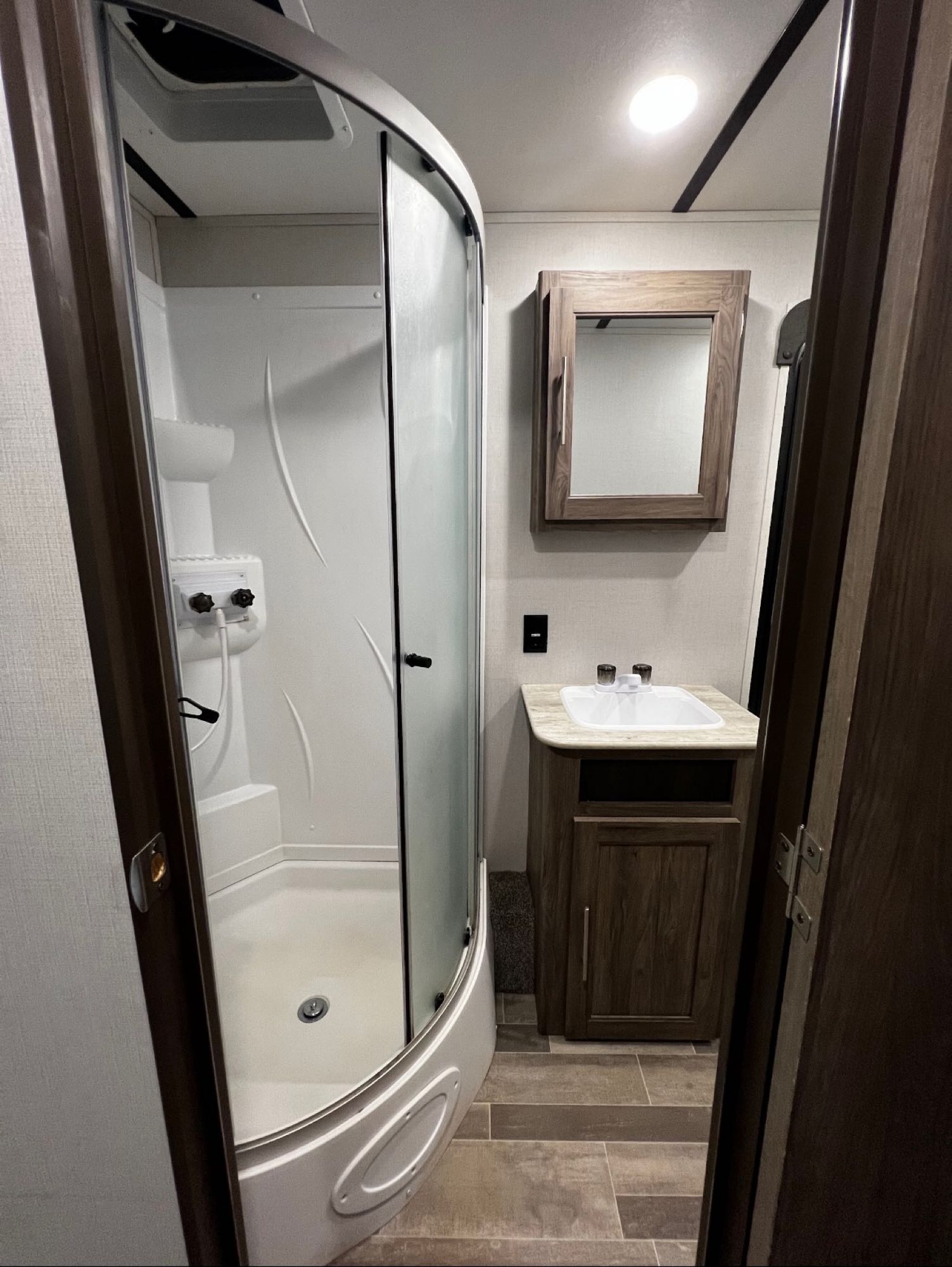 Inside an RV rental bathroom: a curved glass shower stall, wood vanity, sink, and mirror provide comfort on your travels.. Crossroads RV Zinger 2021