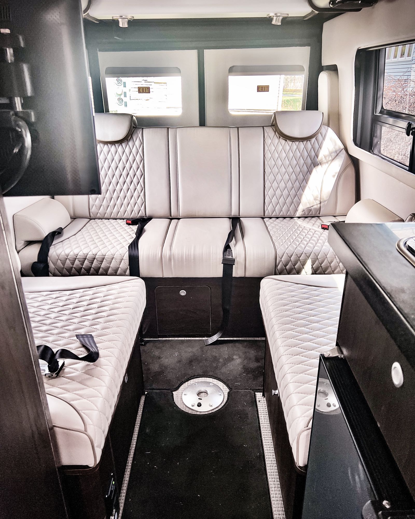 Inside an RV rental: light quilted bench seats facing each other and a rear bench. "EXIT" signs are seen through windows.. Airstream Interstate ‘Slate’ Edition 2019