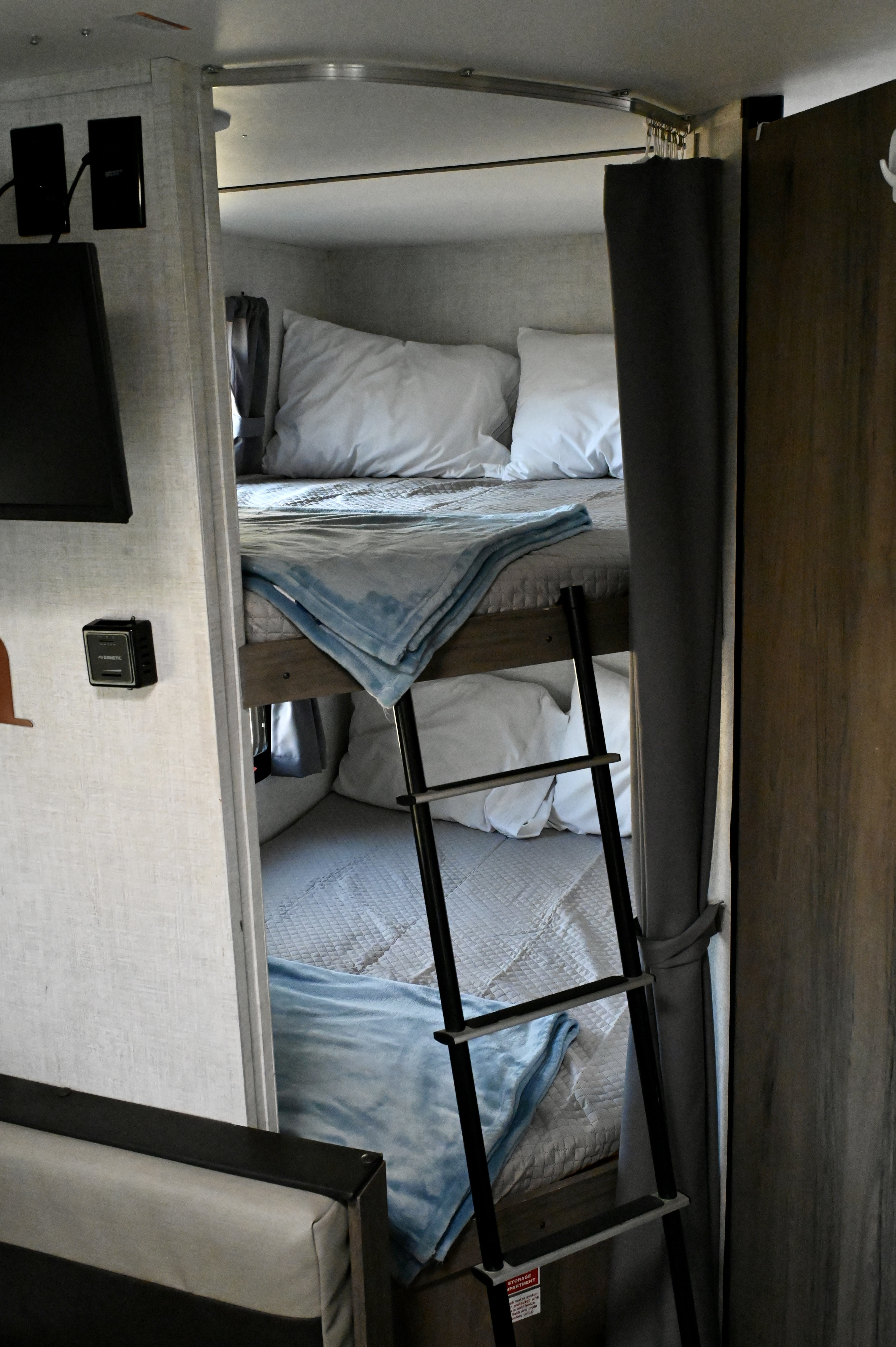 Inside an RV rental, comfortable bunk beds are ready with pillows and blue blankets, featuring a ladder for easy access.. Gulf Stream Ameri-Lite Super Lite 2021