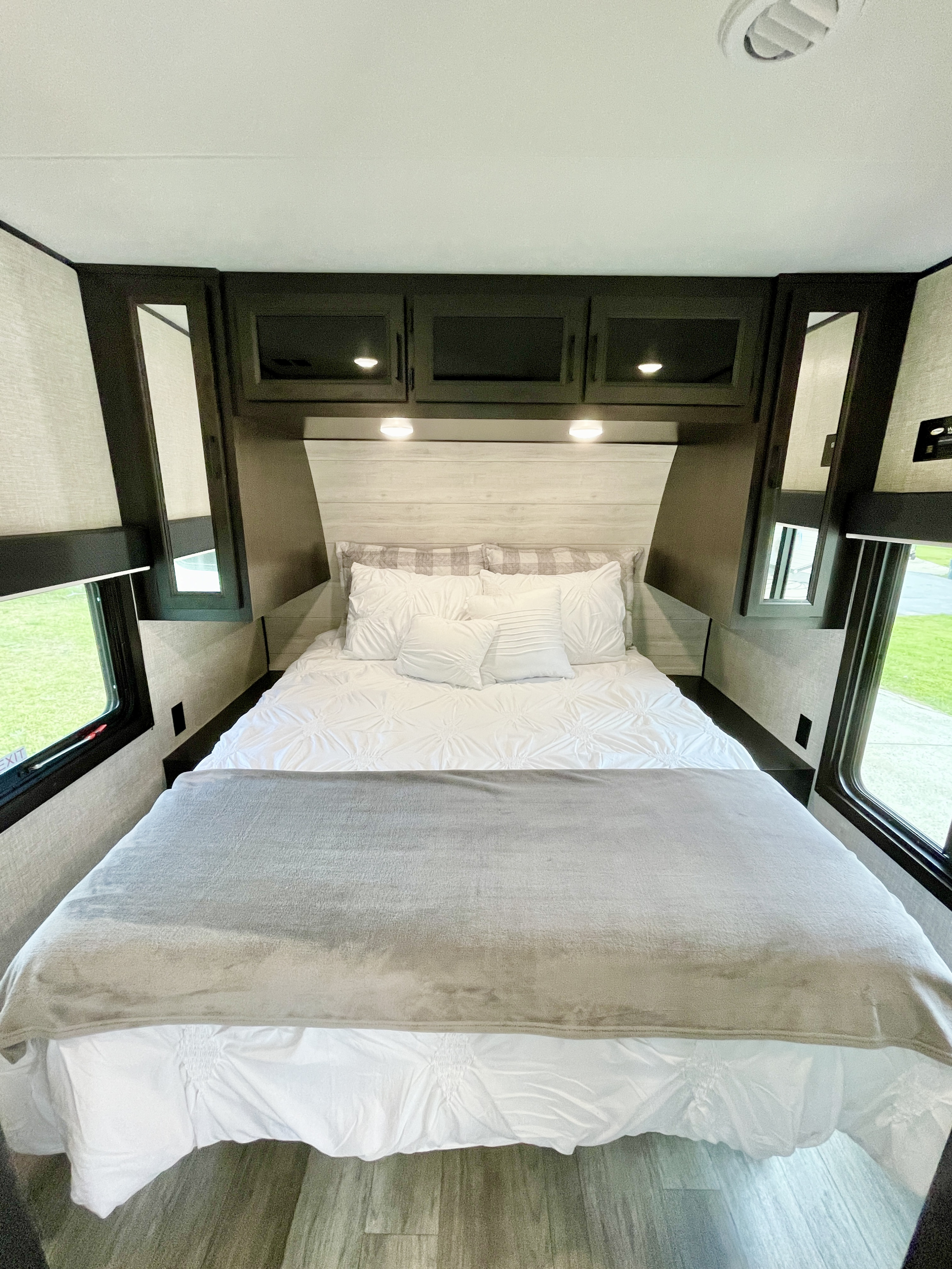 Cozy RV rental bedroom featuring a large bed with white linens, overhead storage, and side windows for natural light.. Jayco Jay Flight 2023