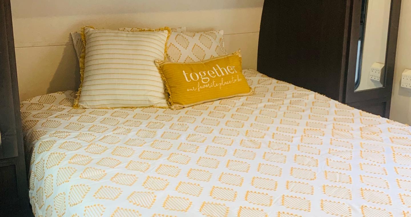 Cozy RV rental bedroom featuring bright yellow & white patterned bedding, including a decorative "together" pillow.. Forest River Stealth 2019
