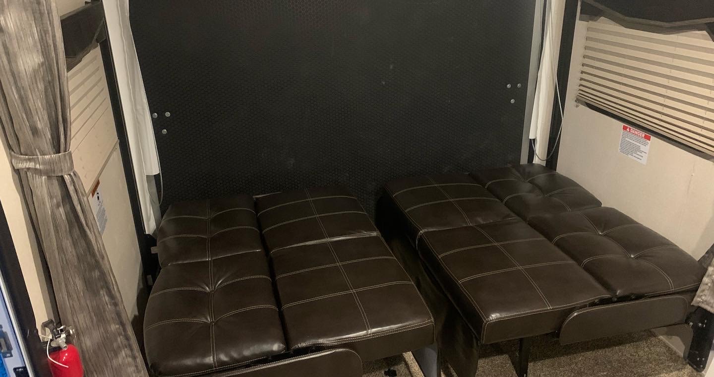 RV rental features two brown futon beds against a dark wall, offering versatile sleeping/lounge space.. Forest River Stealth 2019