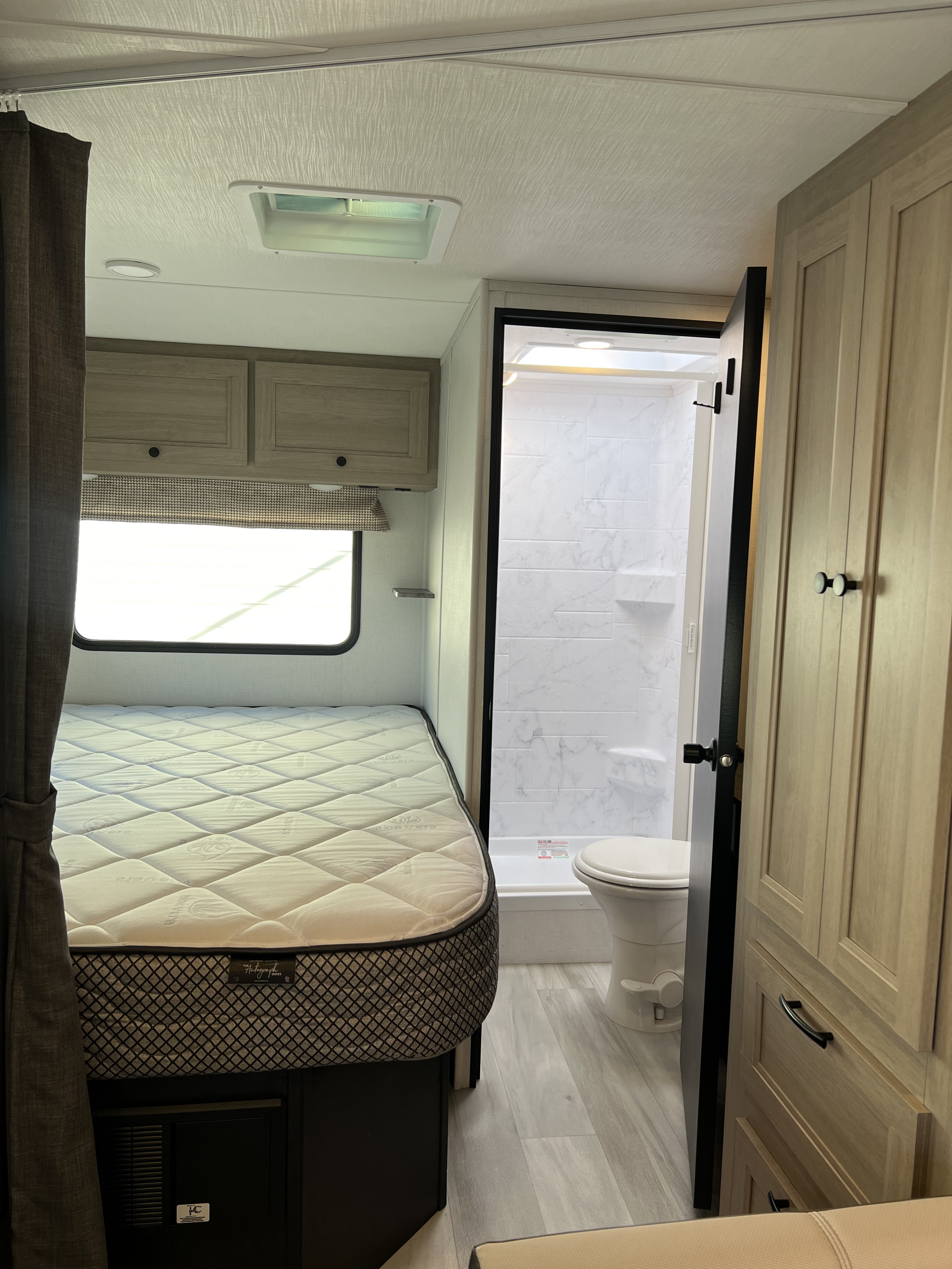 Bright RV rental interior: cozy bedroom with mattress, compact bathroom (shower, toilet), and handy overhead storage.. Forest River Sunseeker 2025