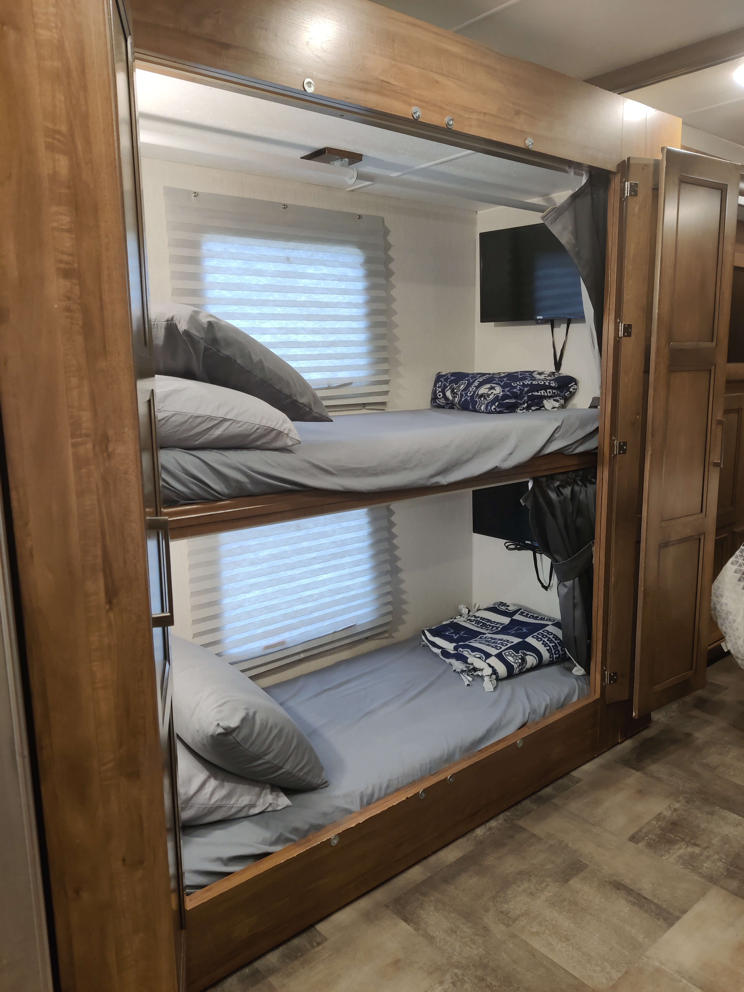 Cozy bunk beds in an RV rental, featuring two tiers with light blue sheets, individual TVs, and windows with blinds.. Forest River Coachmen Mirada 2021