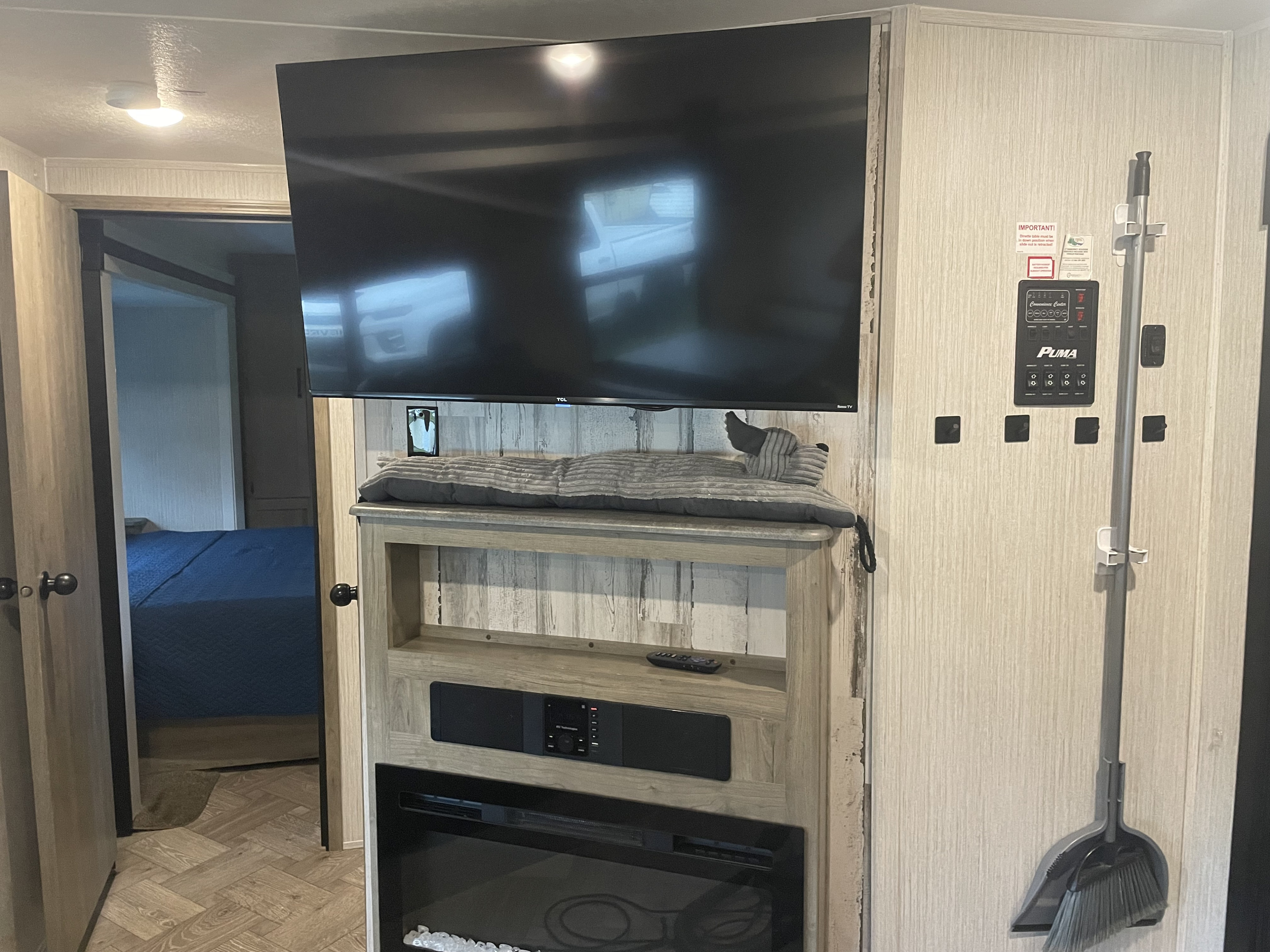 RV rental interior: TV, media console with fireplace, main control panel, and peek into the bedroom.. Forest River Puma 2022