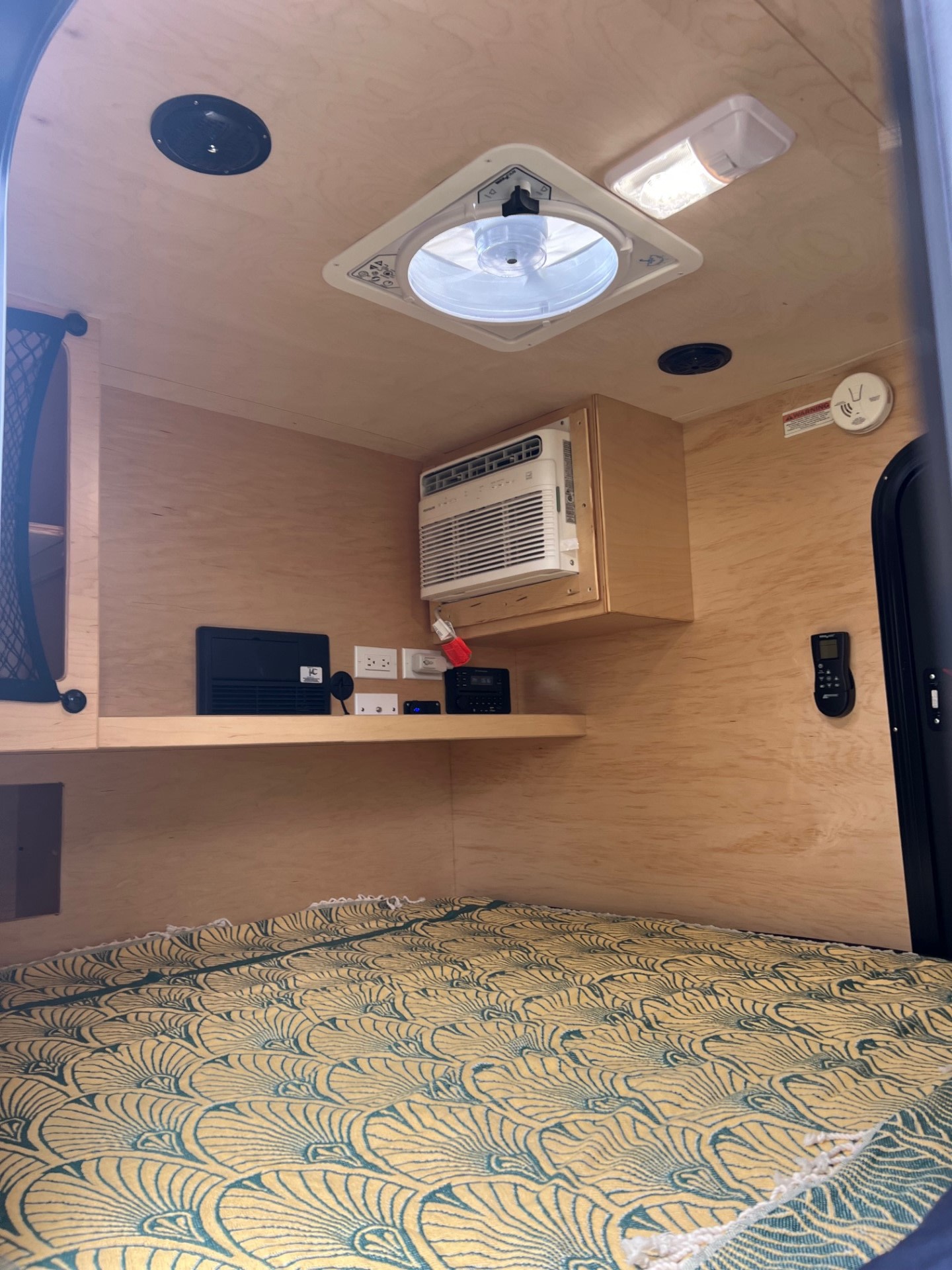 Inside a cozy rv rental: plywood interior with AC, ceiling fan, electronics, and a patterned bed for comfortable travel.. UkanCamp UkanCamp Trailer 2023