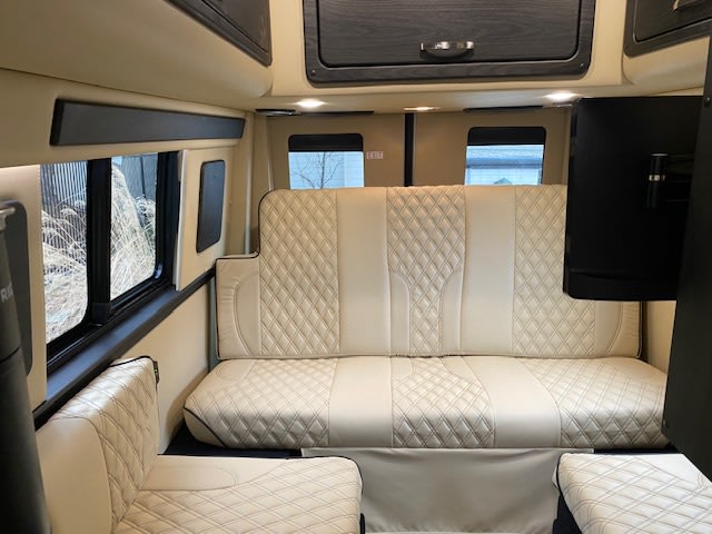 Spacious RV rental interior with cream quilted seating, large windows, and entertainment. Your cozy home on wheels.. Midwest Automotive Designs American Patriot 2023