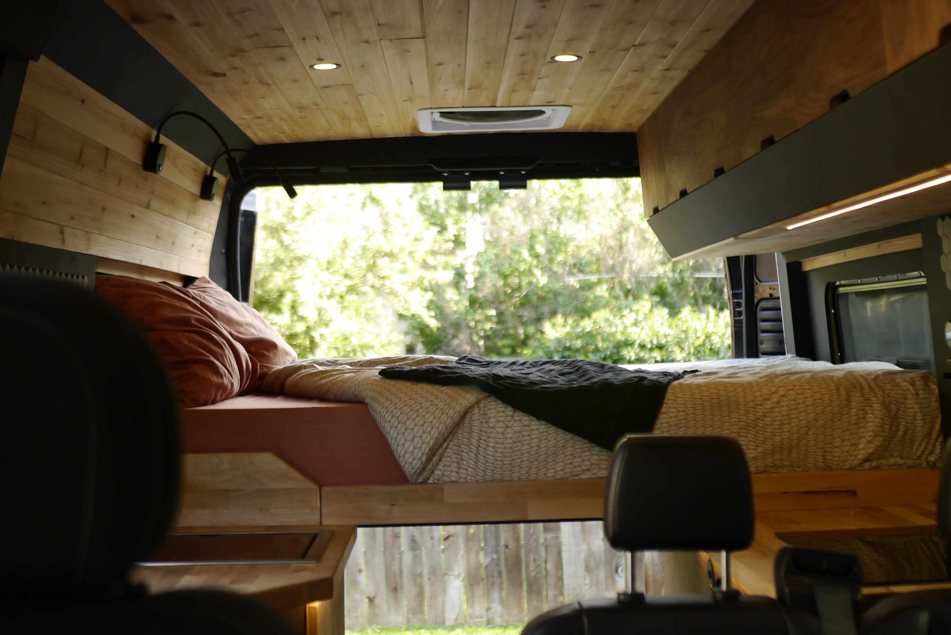 Cozy RV rental camper van interior: wood paneling, comfortable bed, bright lights, and nature views.. Ram Promaster 2019