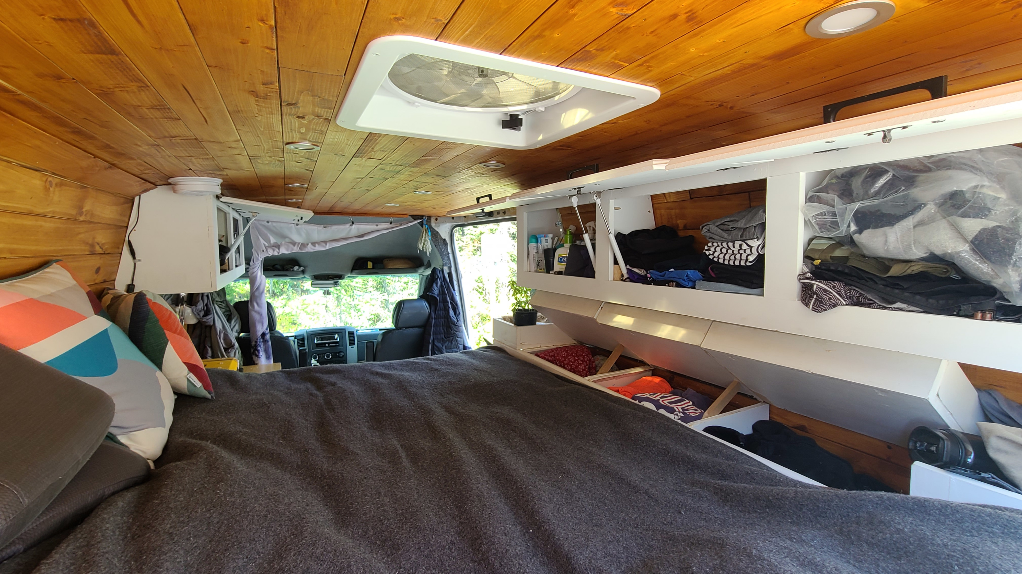 Inside a comfortable RV rental: A warm wooden interior with a bed, overhead storage, and a ceiling fan.. volkswagen sprinter 2007