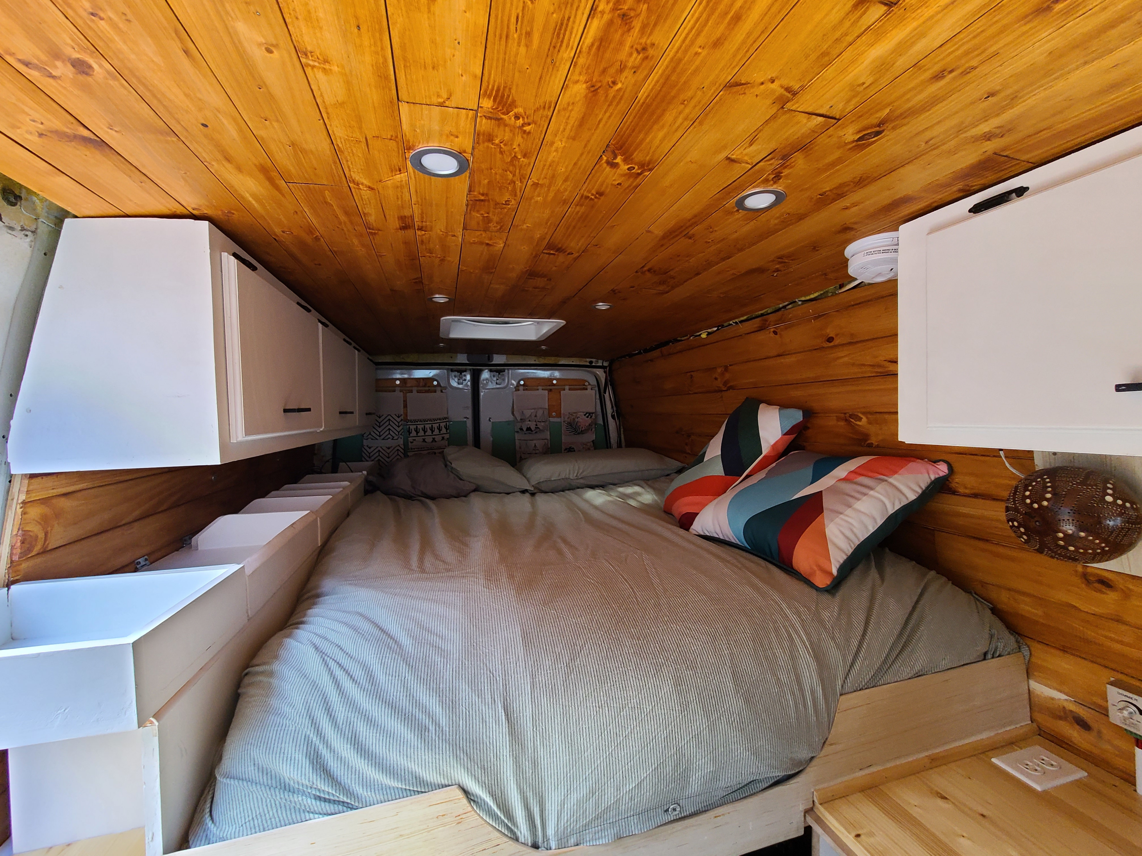 Inside a custom RV rental, featuring a cozy bed, wooden ceiling, and ample storage for comfortable travels.. volkswagen sprinter 2007