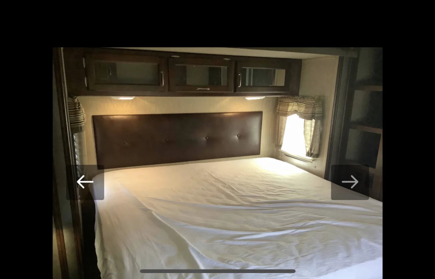 RV rental bedroom with a comfortable bed, padded headboard, and overhead cabinets, typical of an RV interior.. Keystone RV Outback Super-Lite 2016
