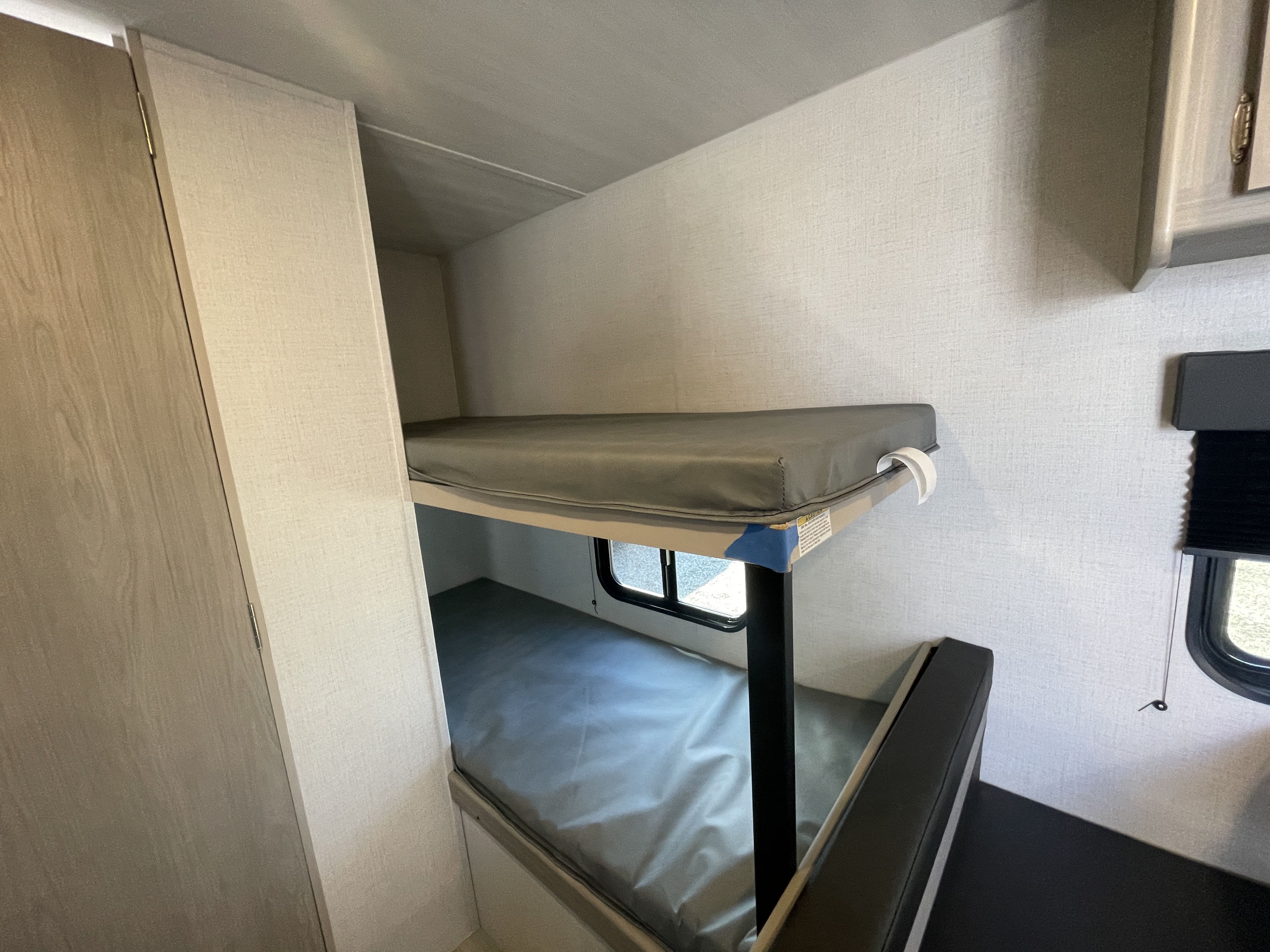 RV rental interior with practical bunk beds. Grey mattresses, window, and cabinet visible in this travel trailer.. Keystone Springdale Classic Mini 2024
