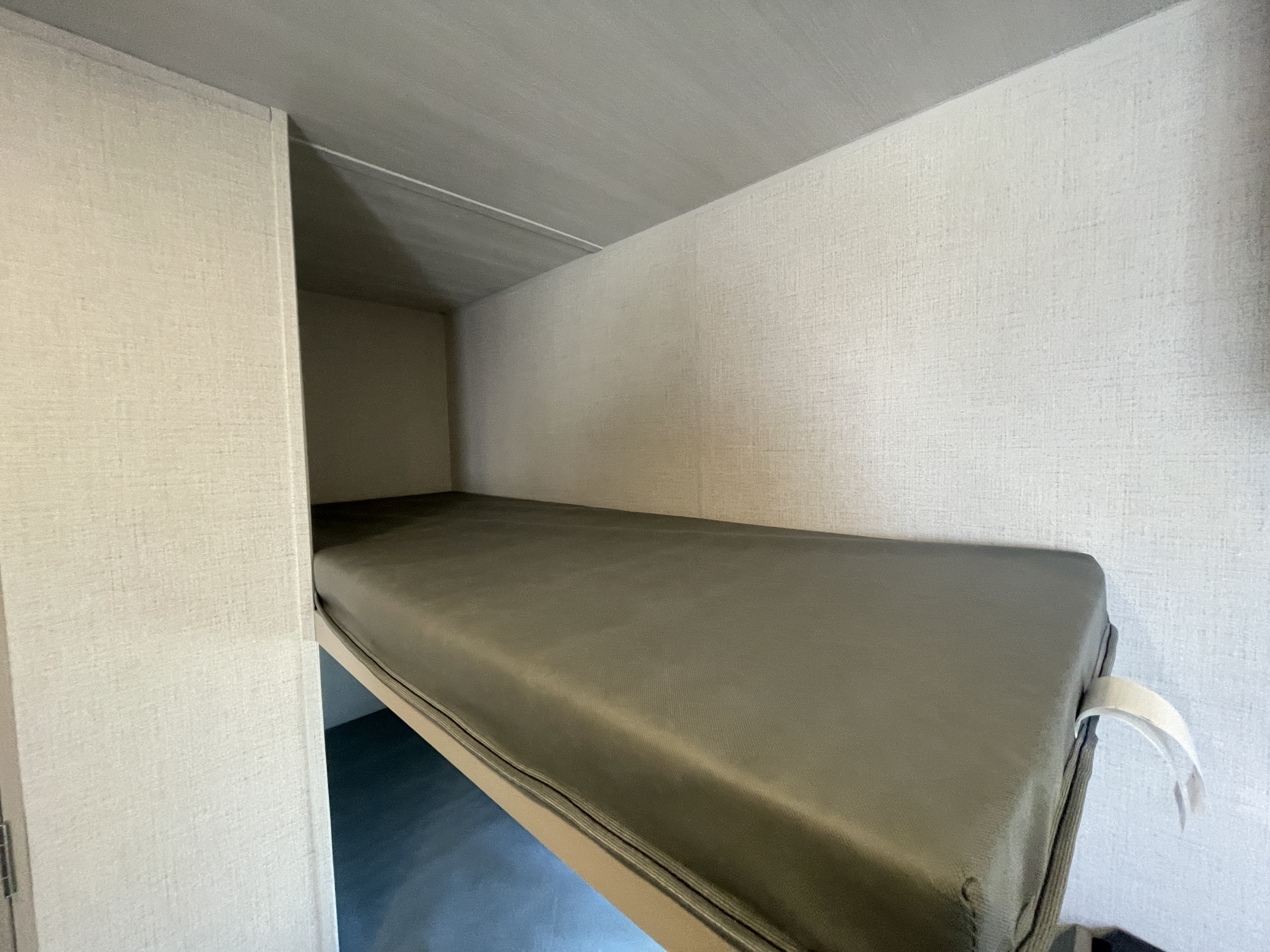 Inside an RV rental: a neat, single bunk bed with a dark gray mattress, ready for rest during your travels.. Keystone Springdale Classic Mini 2024