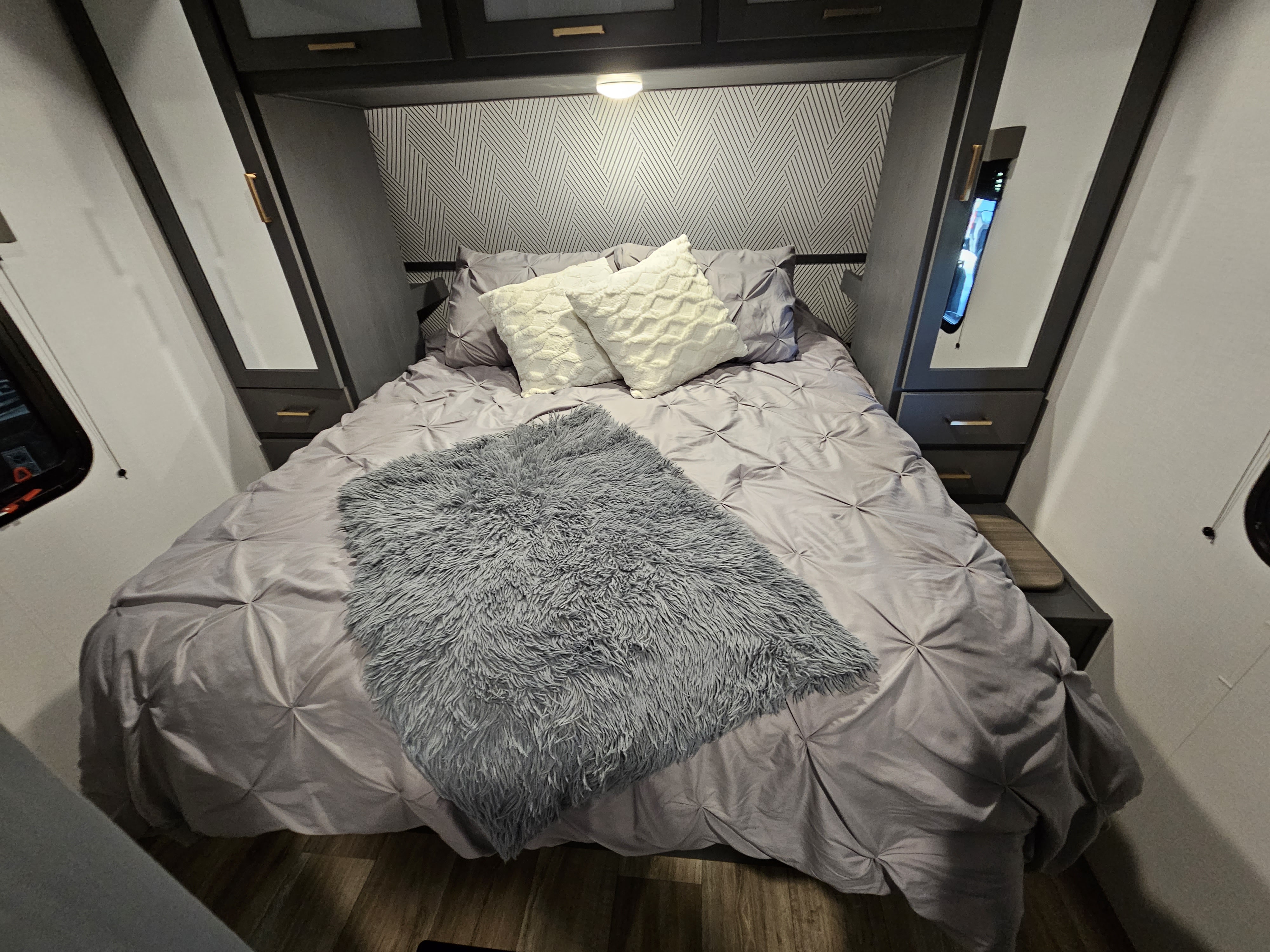 Relax in this modern RV rental bedroom with soft purple bedding, a plush gray throw, sleek dark cabinets, and geometric wallpaper.. Keystone RV Bullet Ultra Lite 2022