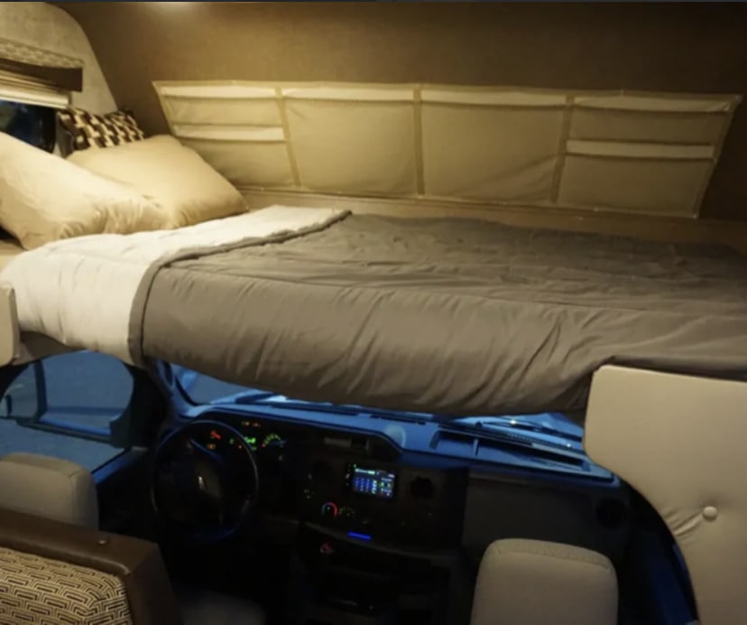 Comfortable over-cab bunk bed in an rv rental, with dashboard visible below. Ideal for a cozy travel adventure.. Adventurer Adventurer Motorhome 2019