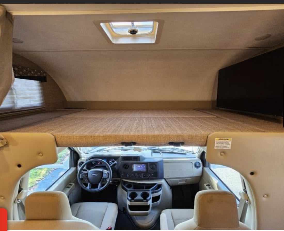 Spacious RV rental interior: overhead bunk, skylight, TV, and cockpit with front seats. Ready for travel.. Thor Freedom Elite 2022
