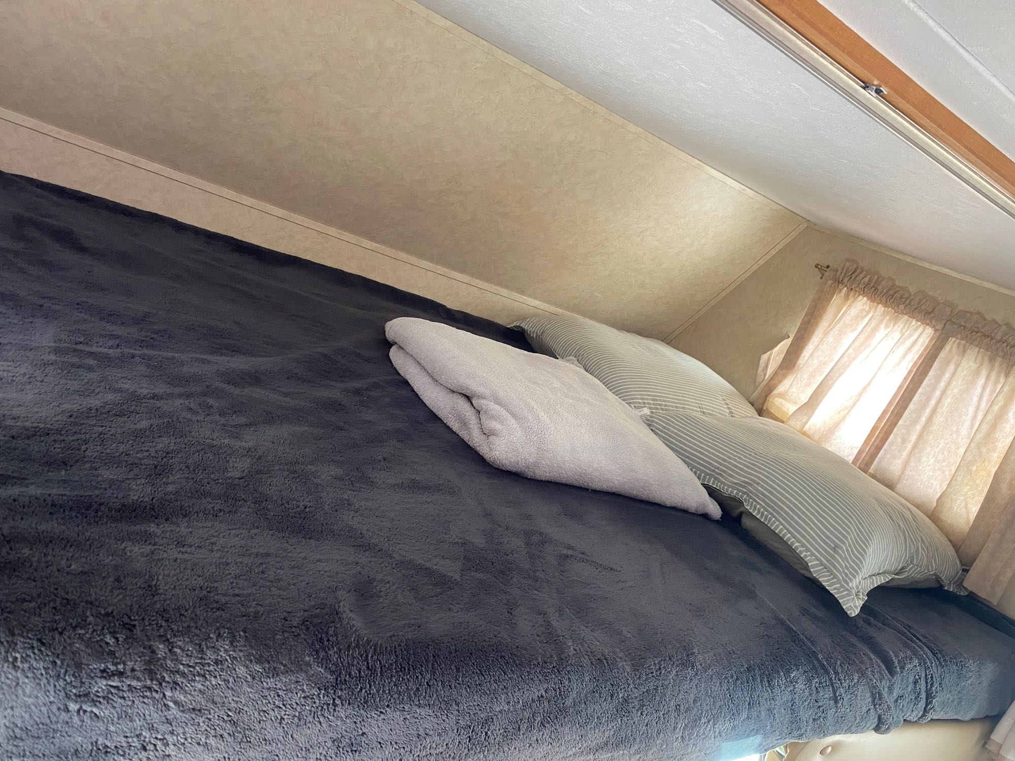 Inside RV rental: Cozy sleeping area with plush dark grey blanket, striped pillows, and a folded throw.. Forest River Sunseeker 2009