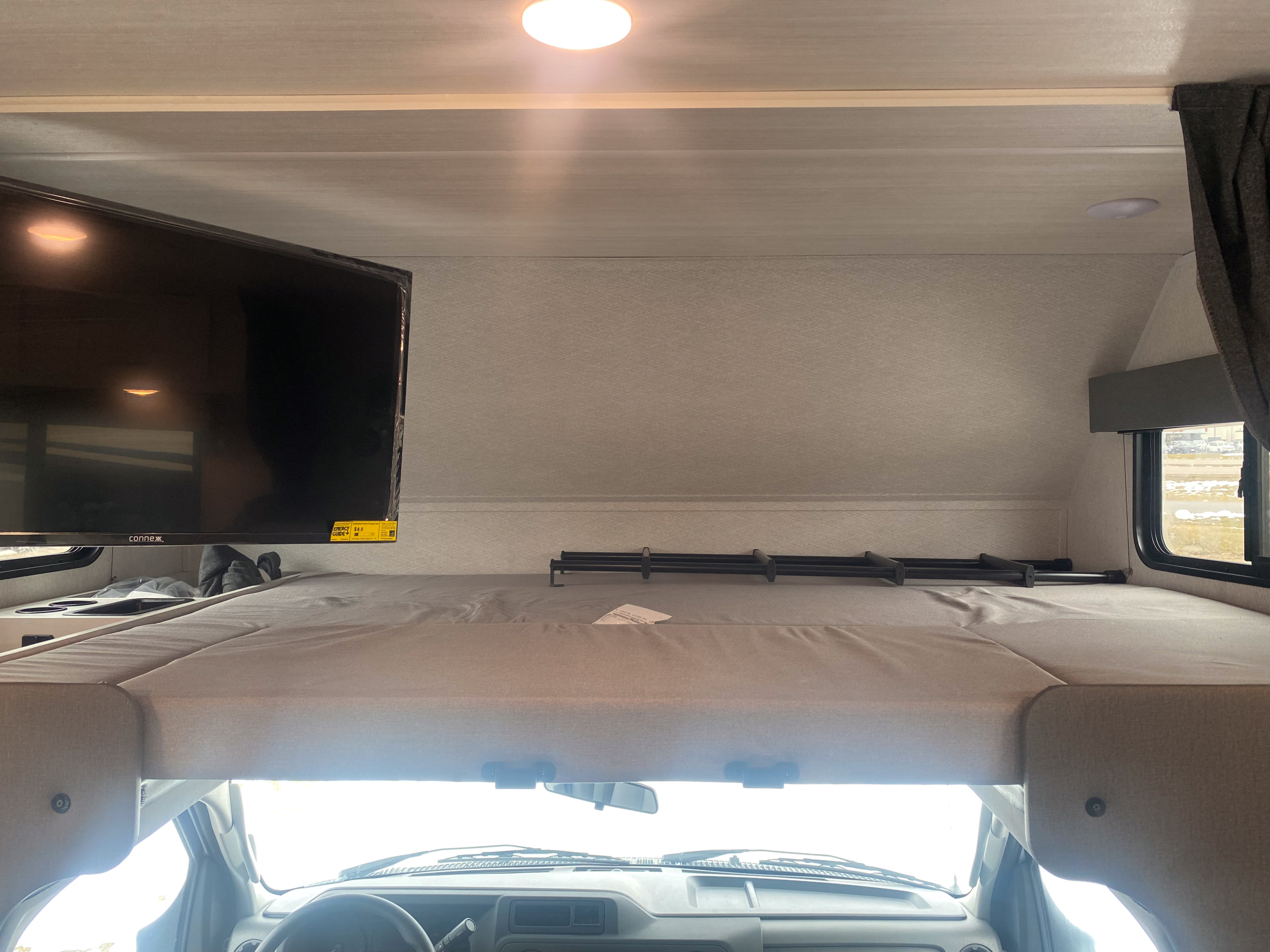 Inside an RV rental: a spacious cab-over bunk with a TV and ladder, overlooking the front windshield.. East to West Entrada 2025