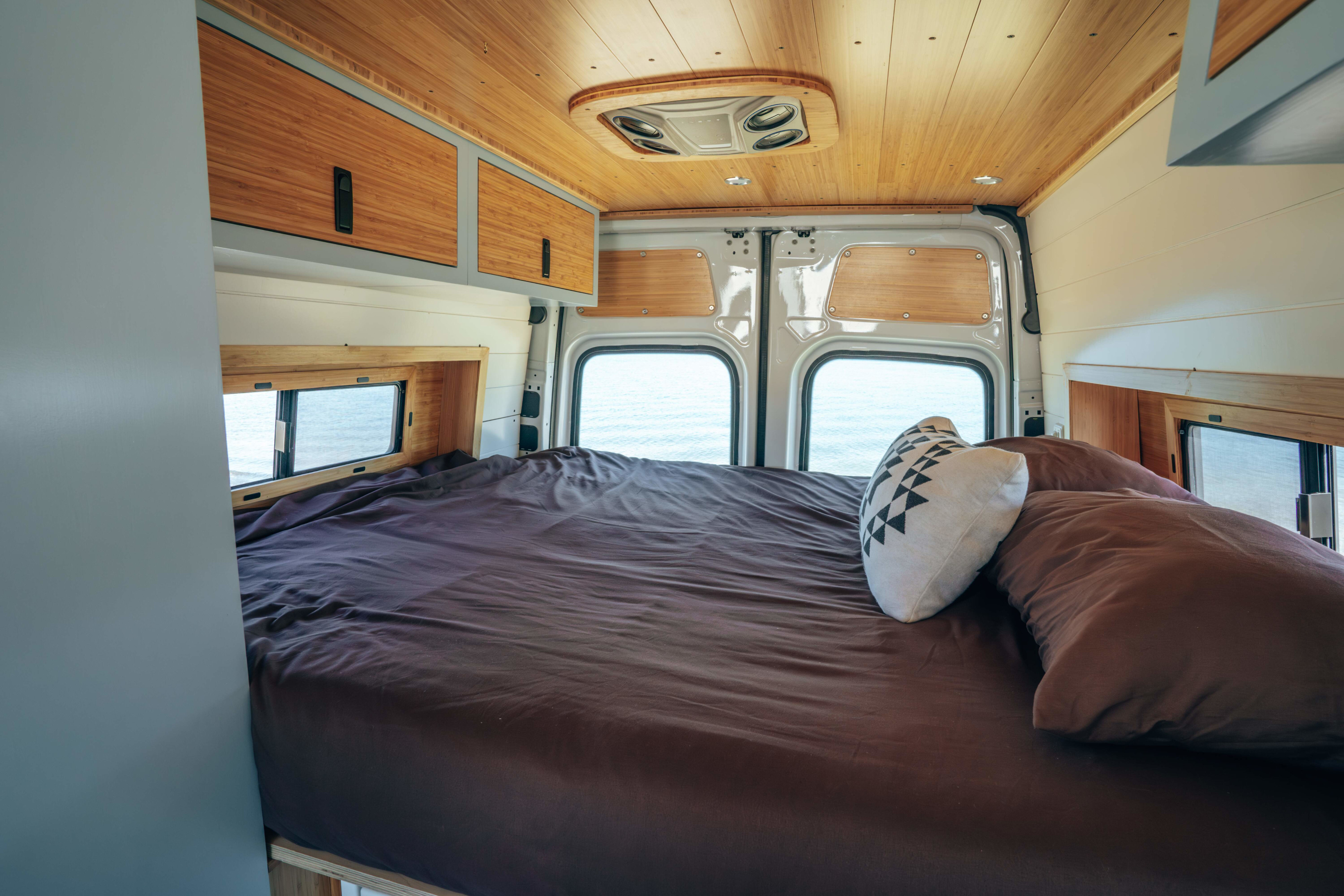 Cozy RV rental interior with a spacious bed and stunning ocean view. Ideal for your next adventure.. Mercedes-Benz Sprinter 2023