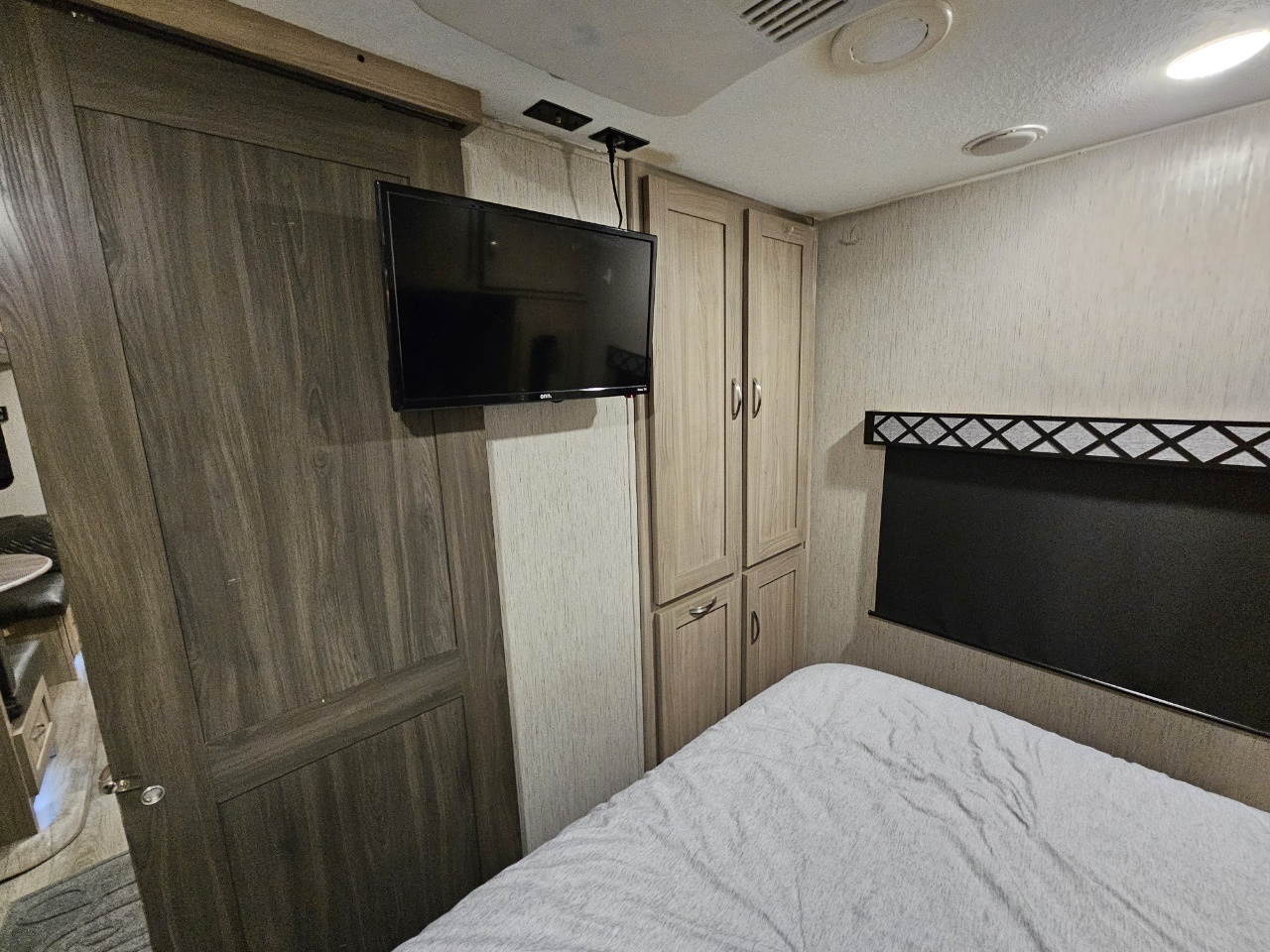 RV rental bedroom shows compact living: wall TV, wooden cabinets, and bed with light gray bedding.. Coachmen 326BHDSLE 2022