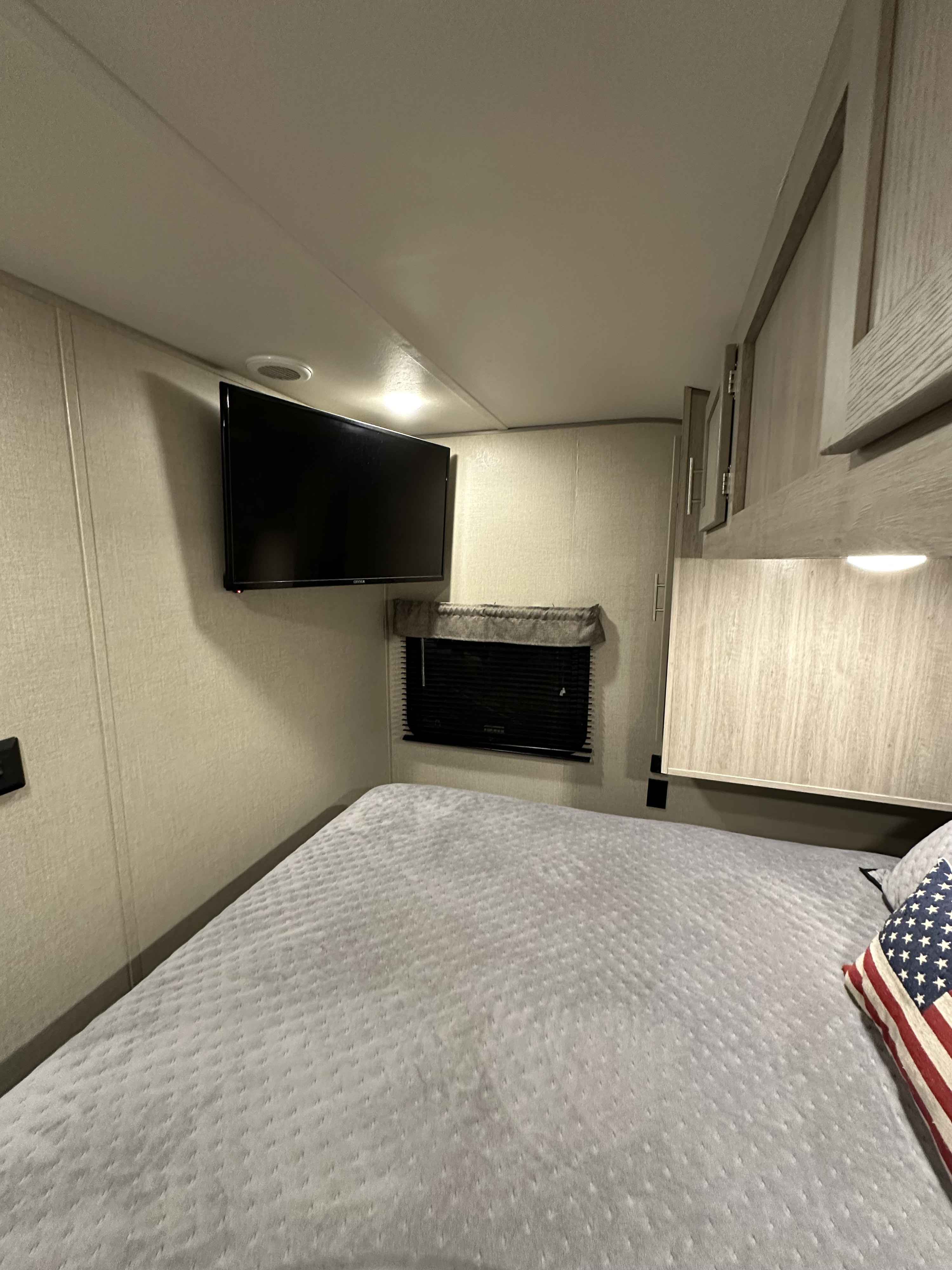This RV rental's bedroom features a mounted TV, window with blinds, and a cozy bed, ideal for relaxation.. Coachmen Catalina Legacy Edition 2022