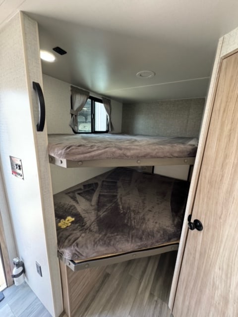 This RV rental interior showcases a cozy bunk bed setup, complete with linens, a window, and essential controls.. Winnebago Minnie Winnie 2021