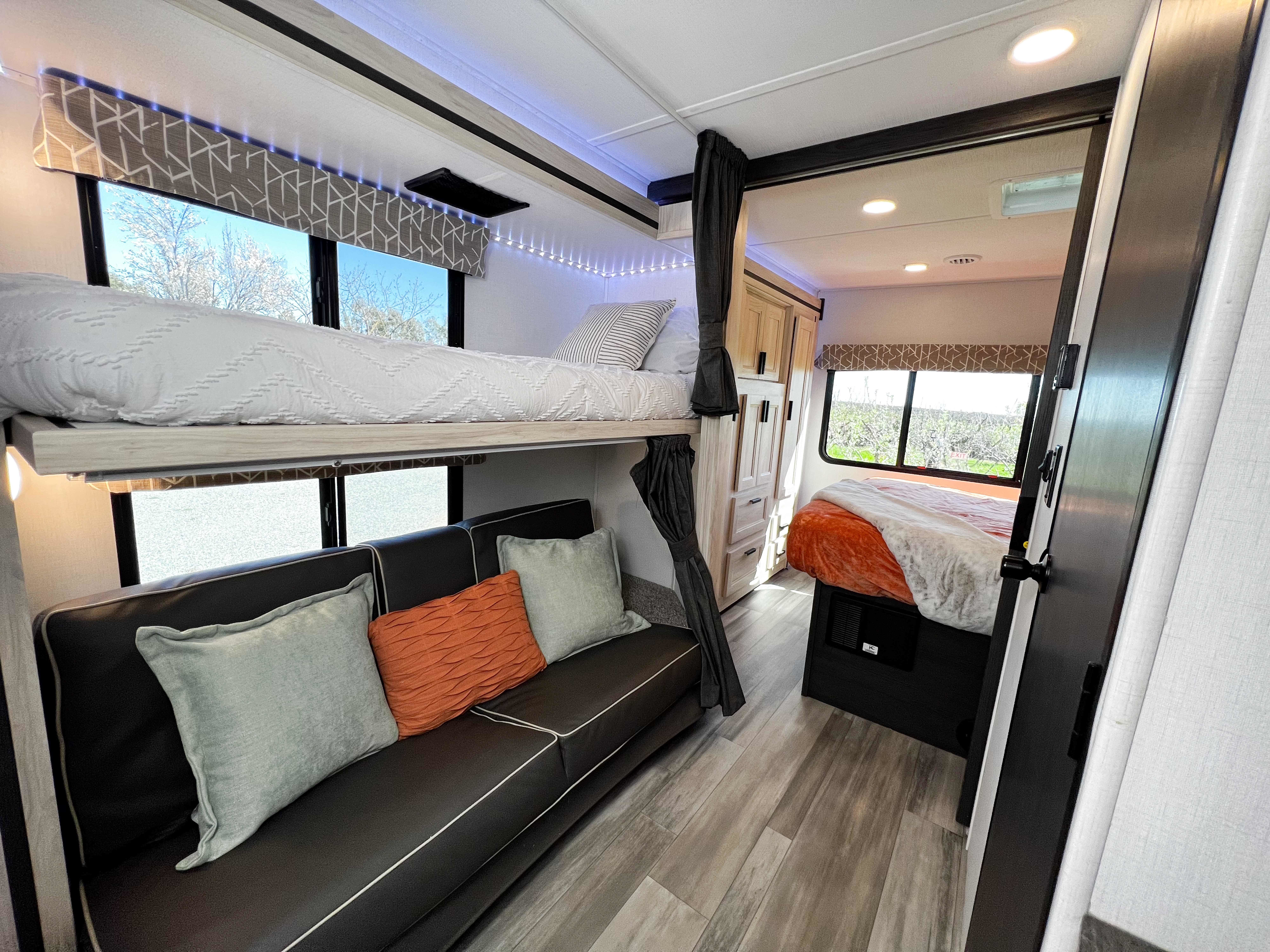 Comfortable RV rental interior with a bunk bed over a sofa, leading to a private master bedroom, illuminated by modern lighting.. Forest River Sunseeker LE 2023