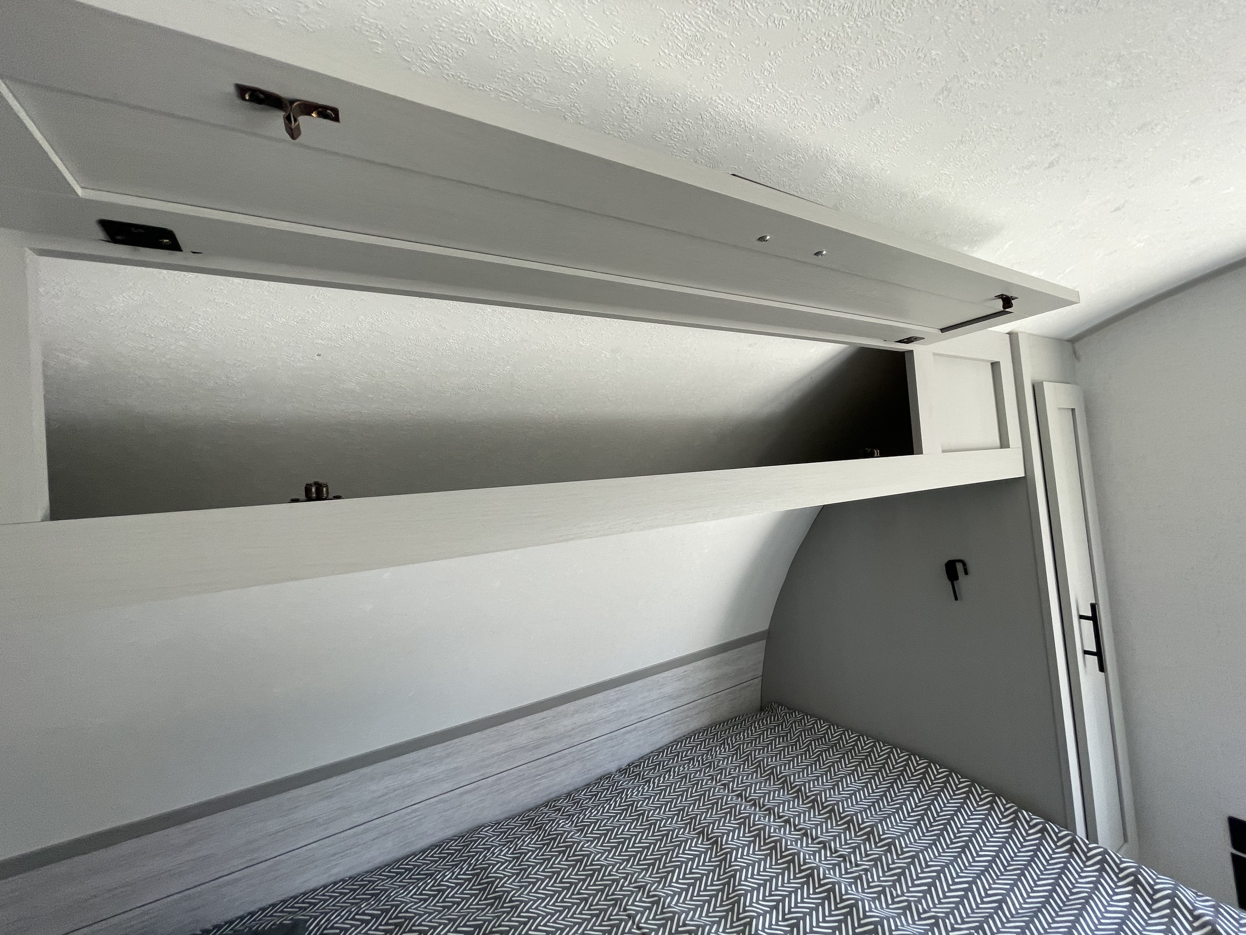 Modern RV rental bedroom showcasing open overhead storage, a patterned bed, and efficient built-in cabinets for travel.. Forest River Salem FSX PLATINUM 2021