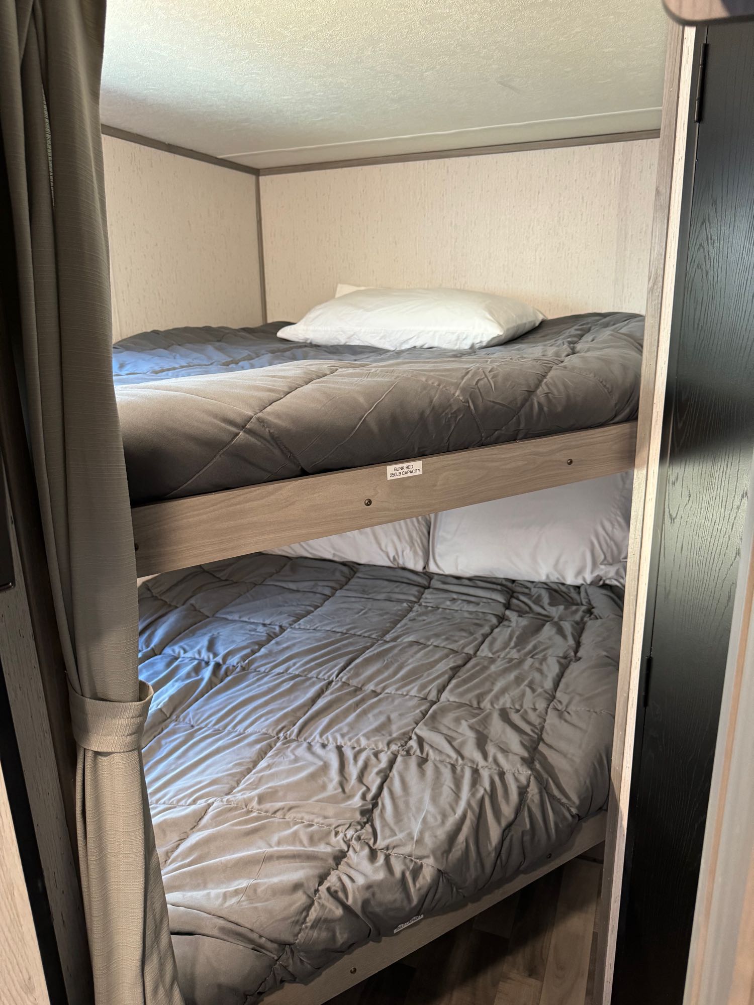 This RV rental features cozy bunk beds with grey comforters and white pillows, perfect for family adventures on the road.. Dutchmen Kodiak SE 2022