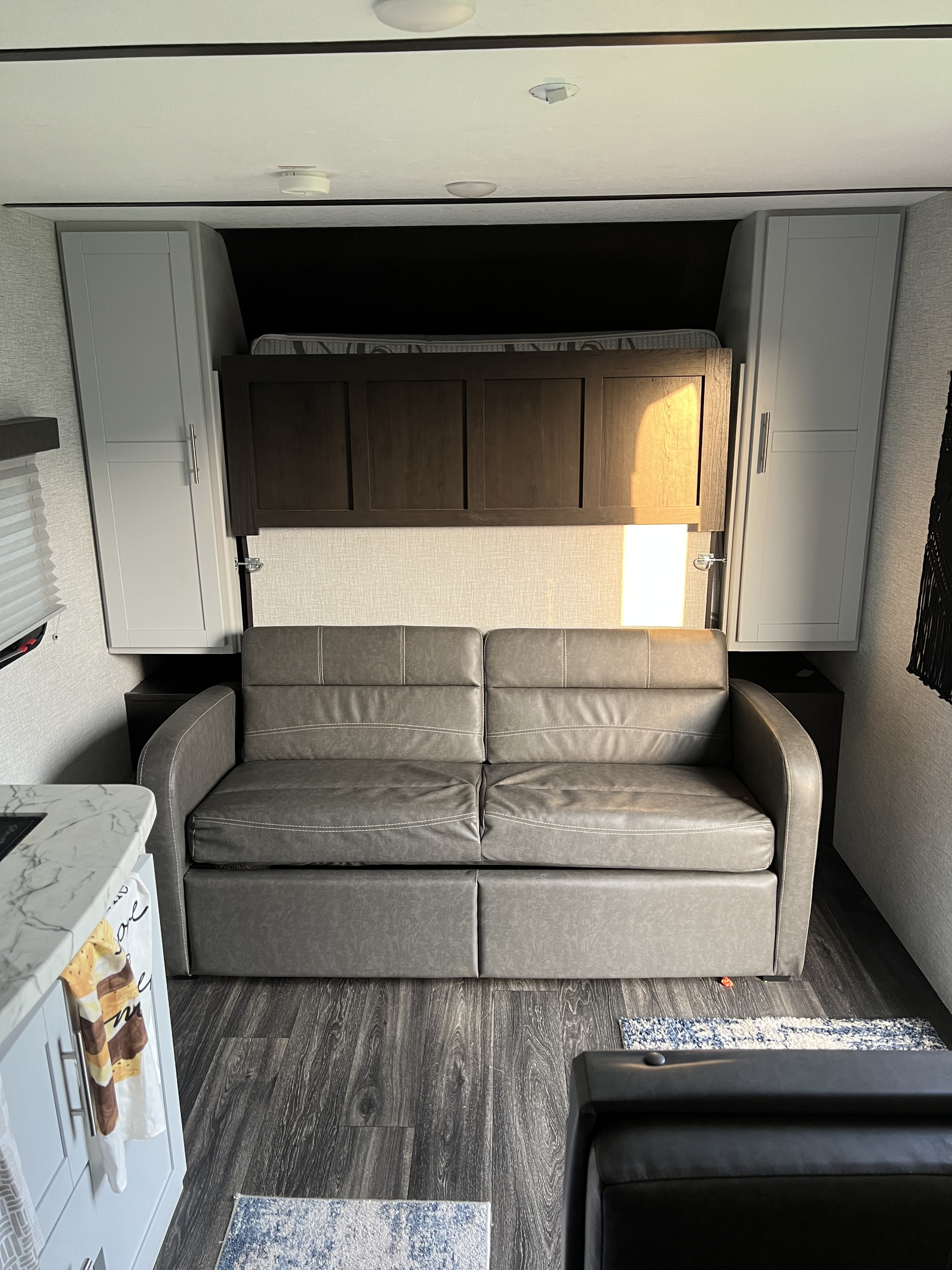 Modern RV rental living area with a versatile sofa bed, overhead cabinets, and wood-look flooring.. Keystone RV Bullet Crossfire 2021