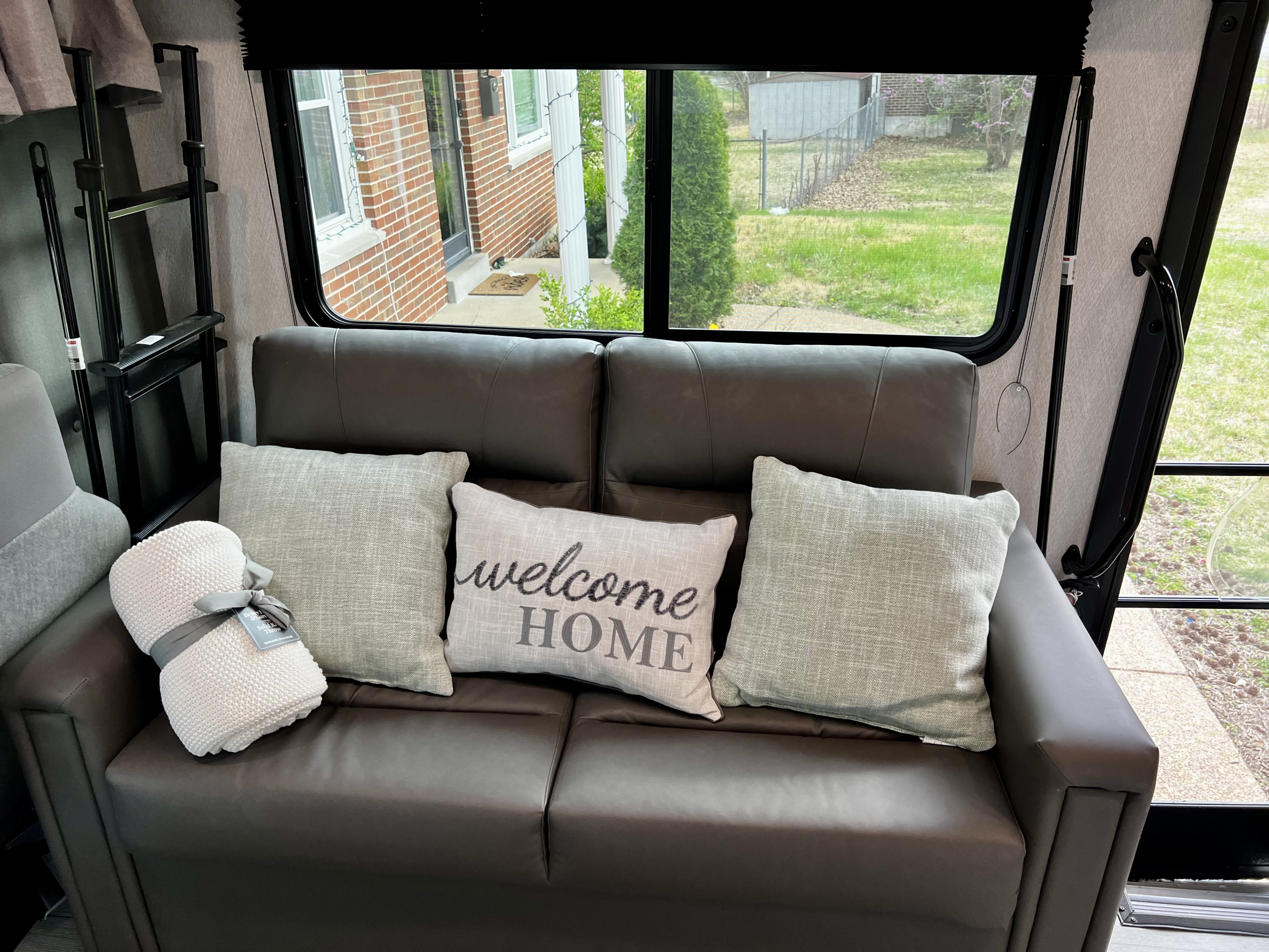 Inside an RV rental: a comfortable sofa with 'welcome home' pillow, blanket, and serene window view. Your cozy travel space.. 1FDXE4FN9RDD14726 3100FB 2023