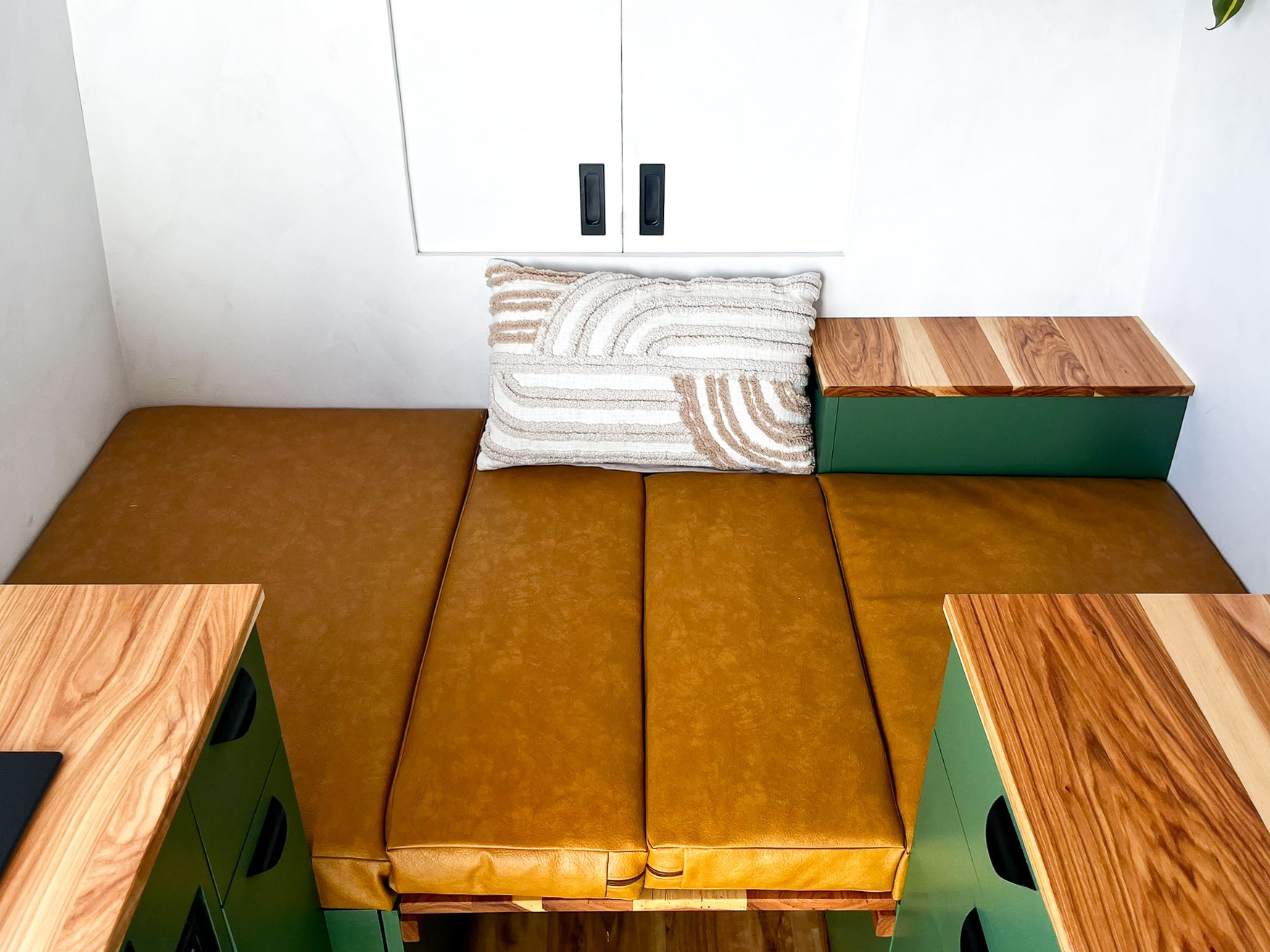 Cozy RV rental interior showing a tan cushioned seating/bed area, white walls, and green storage with wood tops.. Mercedes Sprinter 2023