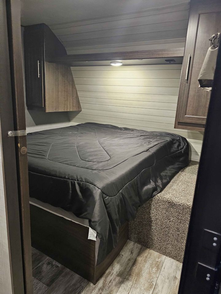Explore this compact RV rental bedroom featuring a neatly made bed, overhead cabinets, and warm lighting.. Crossroads Zinger 2018