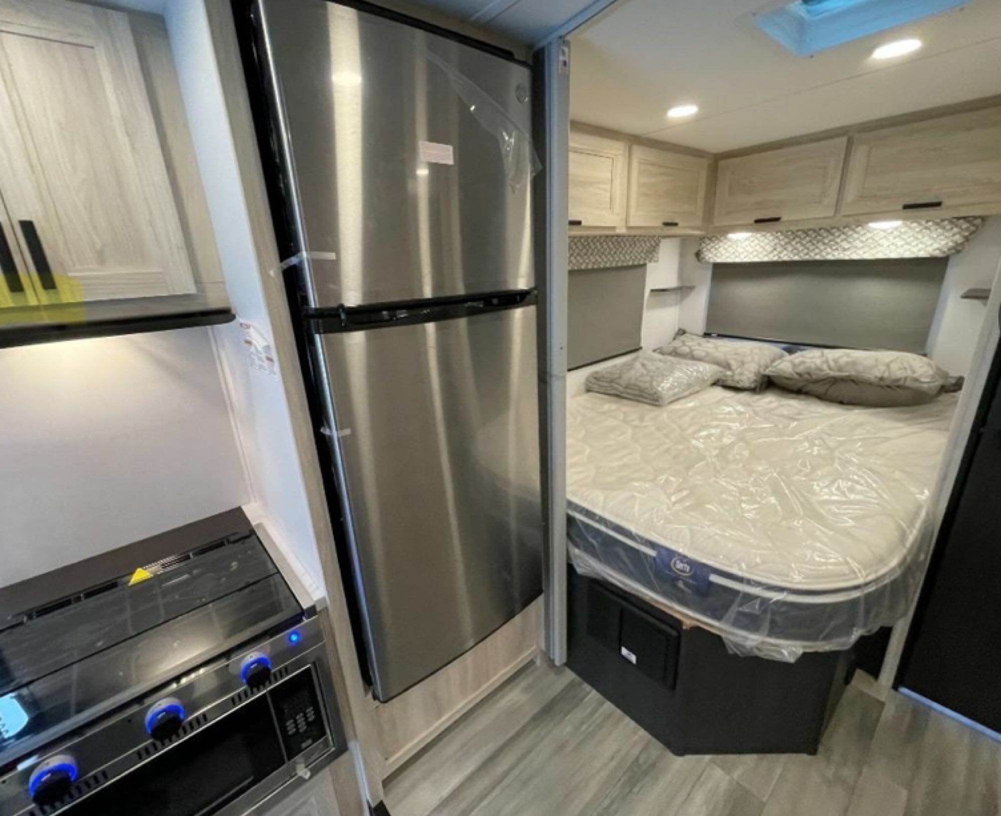 Inside this RV rental: a modern kitchen with a stainless fridge & stove, plus a cozy bed with overhead storage.. Forester LE 2023
