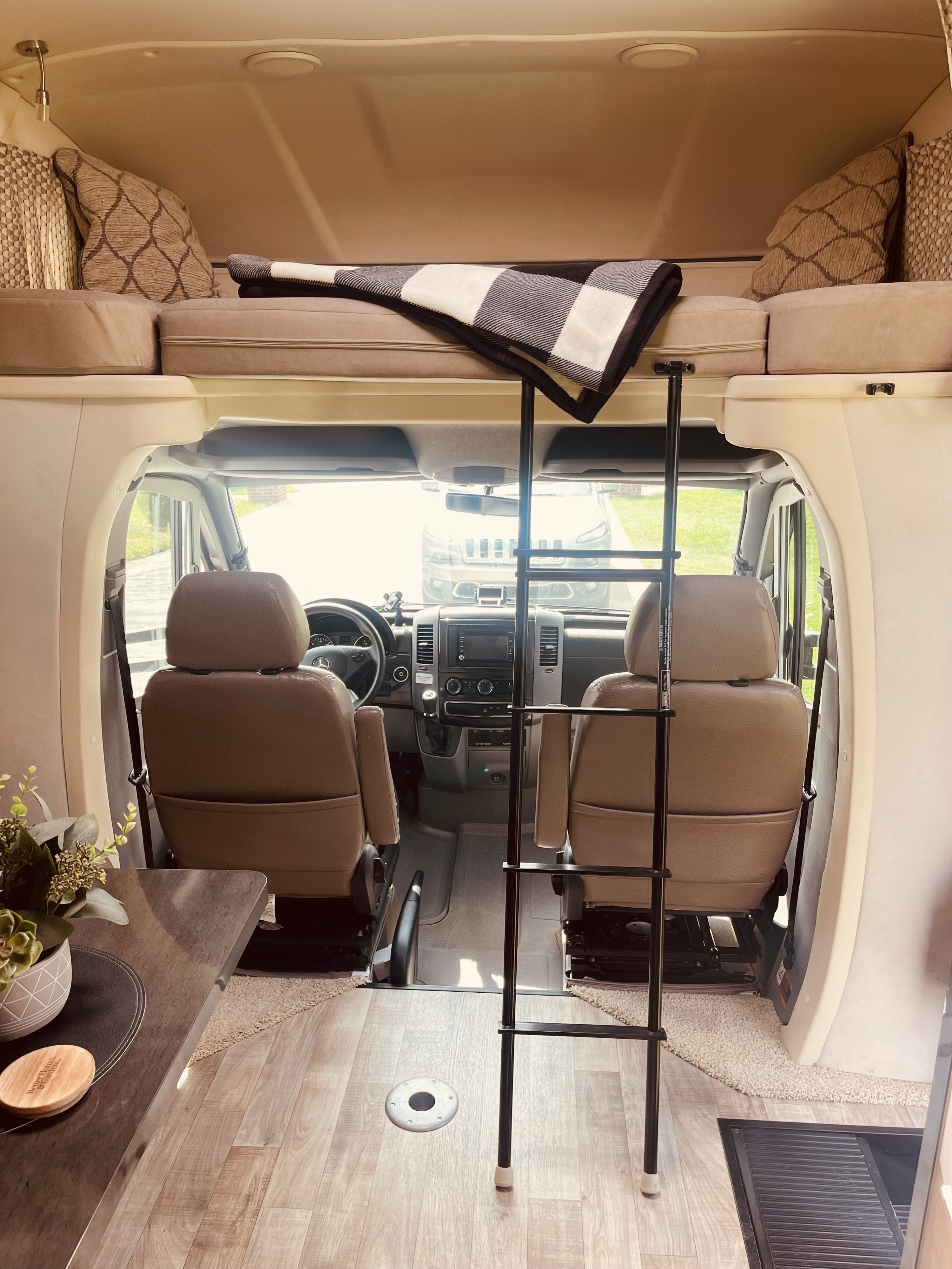 View of an RV rental interior, from living area to front cockpit. Features a cozy over-cab bunk with ladder & patterned decor.. Winnebago View 2016
