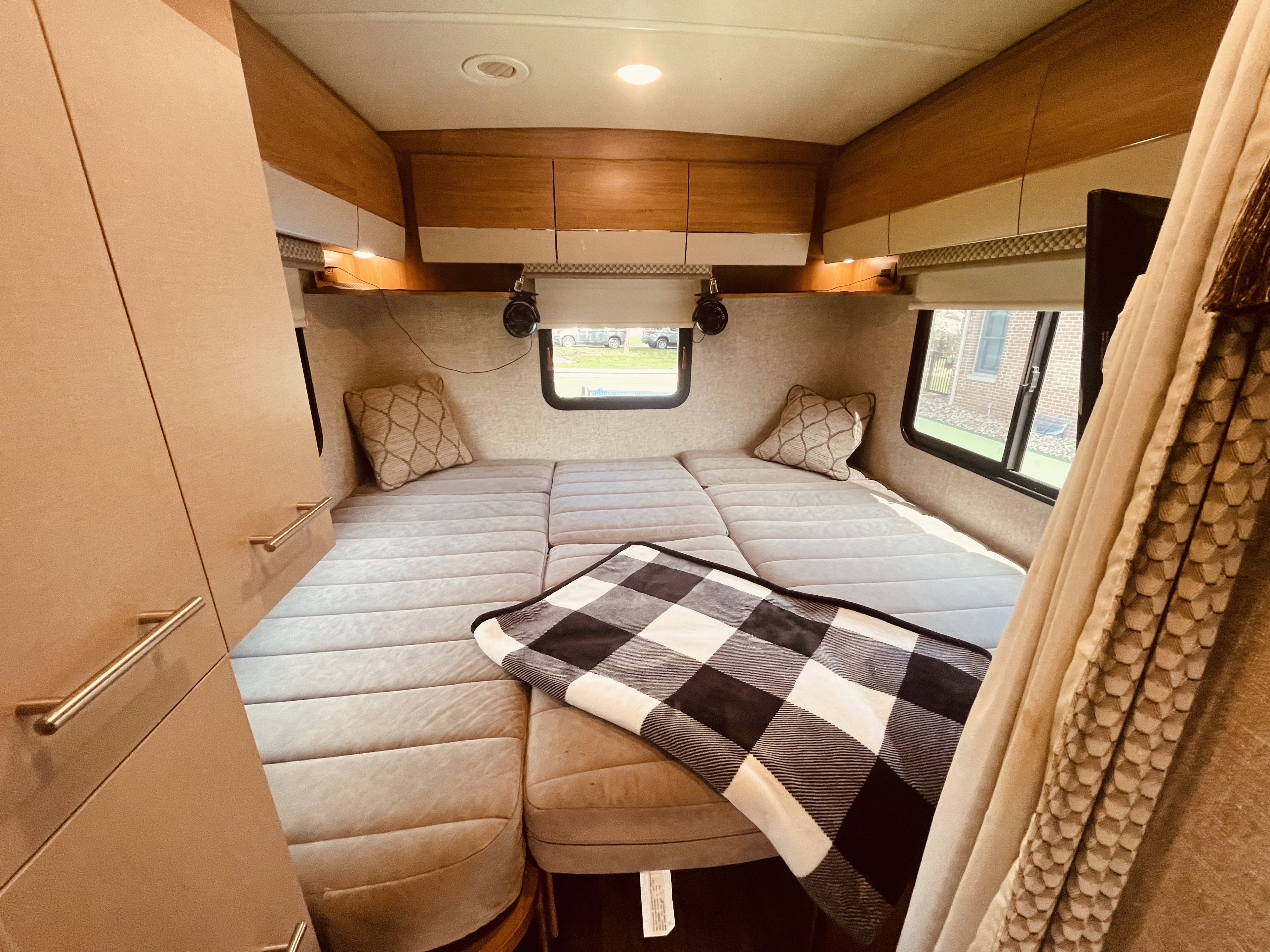 Spacious RV rental bedroom with a large bed, pillows, and buffalo check blanket, featuring overhead storage and windows.. Winnebago View 2016