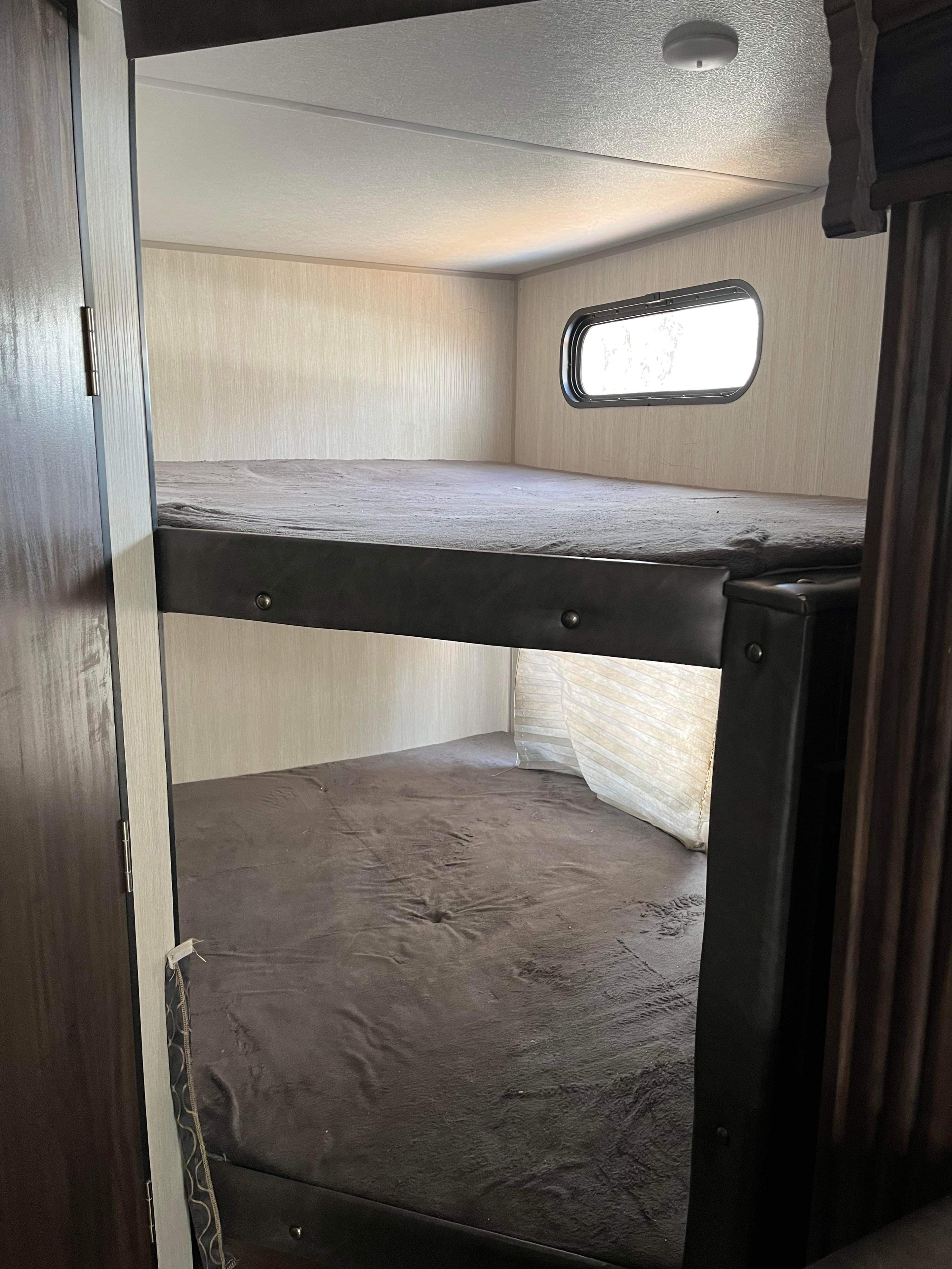 Inside an RV rental: cozy bunk beds with dark bedding, a small window, and light fixtures.. Forest River Cherokee Grey Wolf 2020