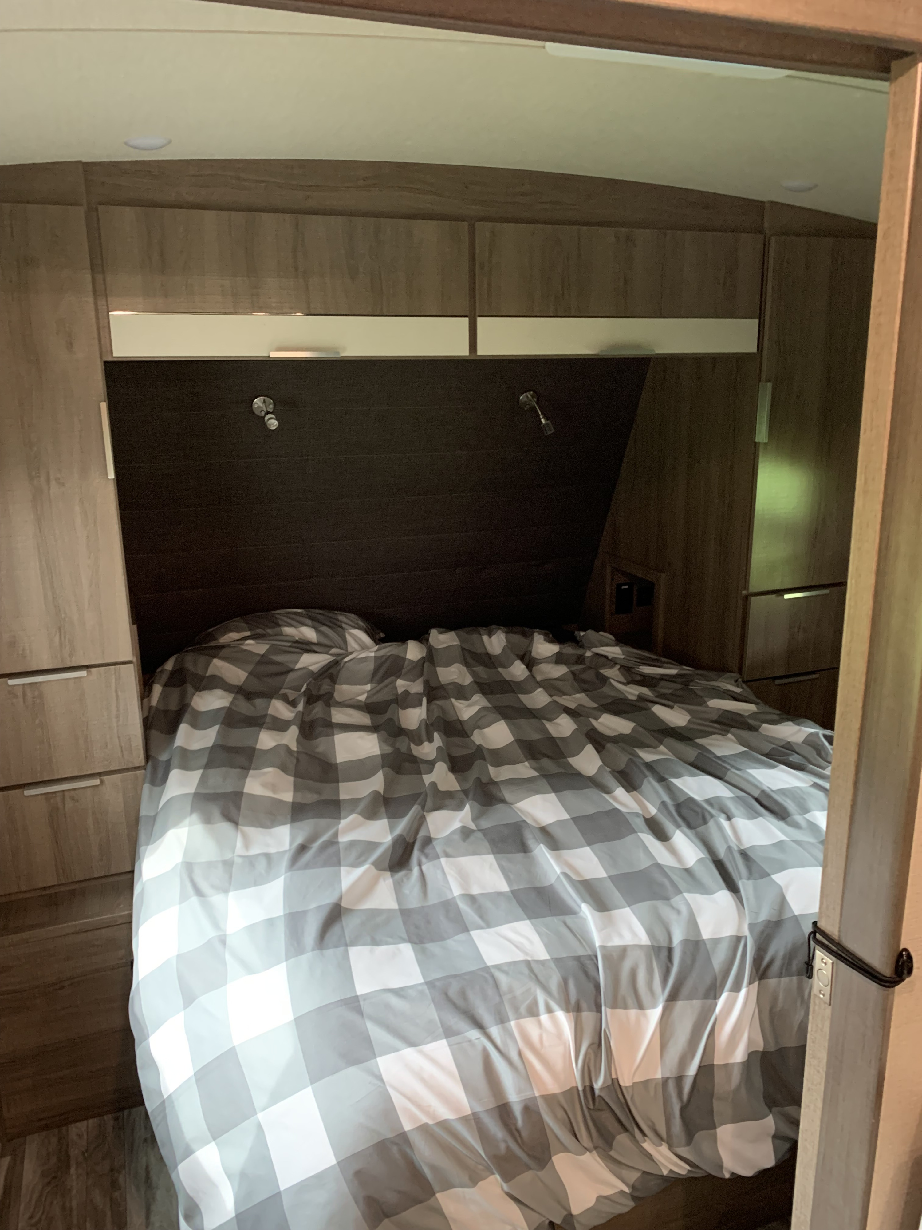This RV rental bedroom features a comfy checkered bed, reading lights, and ample built-in storage.. Grand Design Imagine 2021