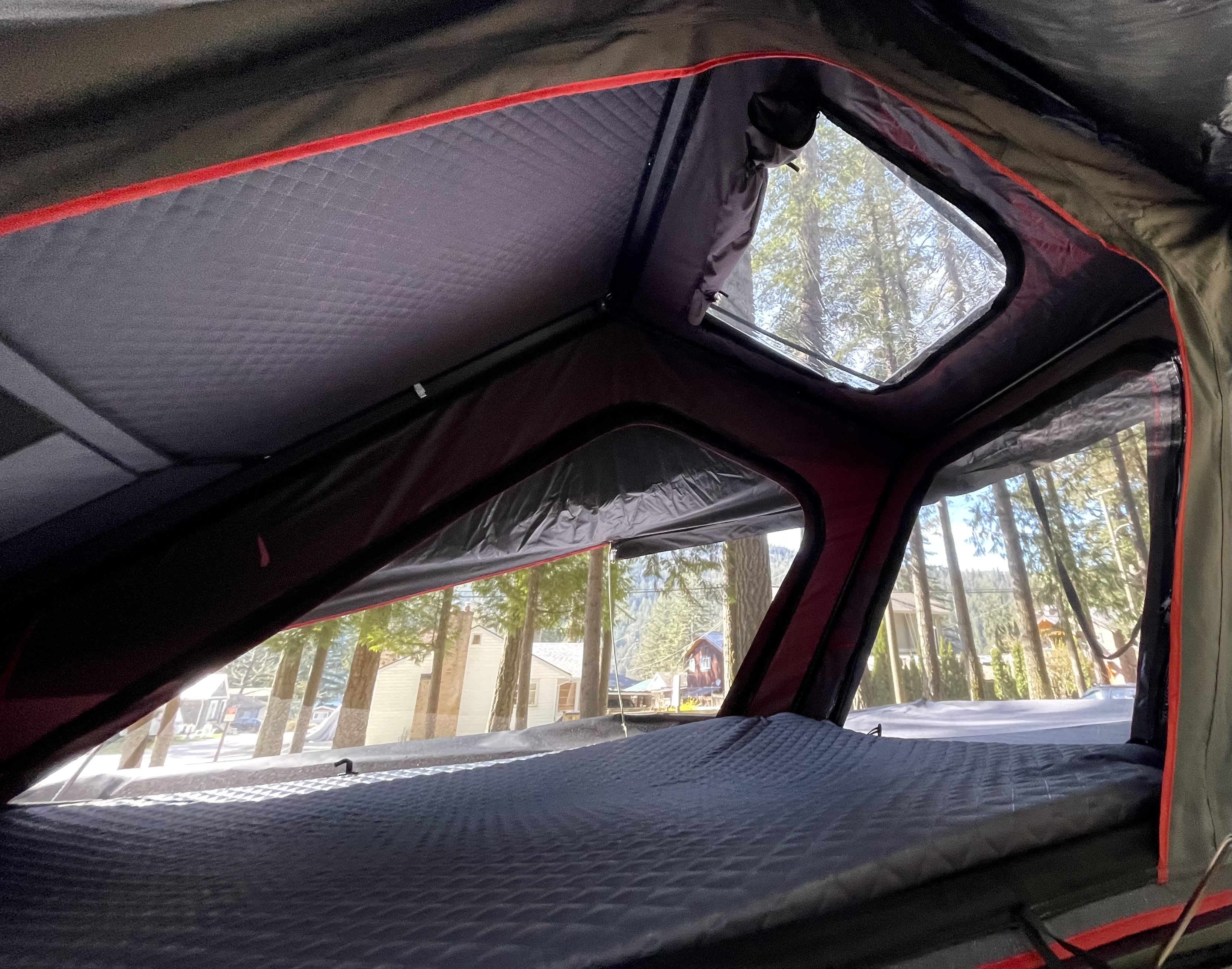 Cozy quilted mattress inside a rooftop tent, offering clear views of trees and houses. Ideal for your rv rental adventure.. Toyota FJ 2007