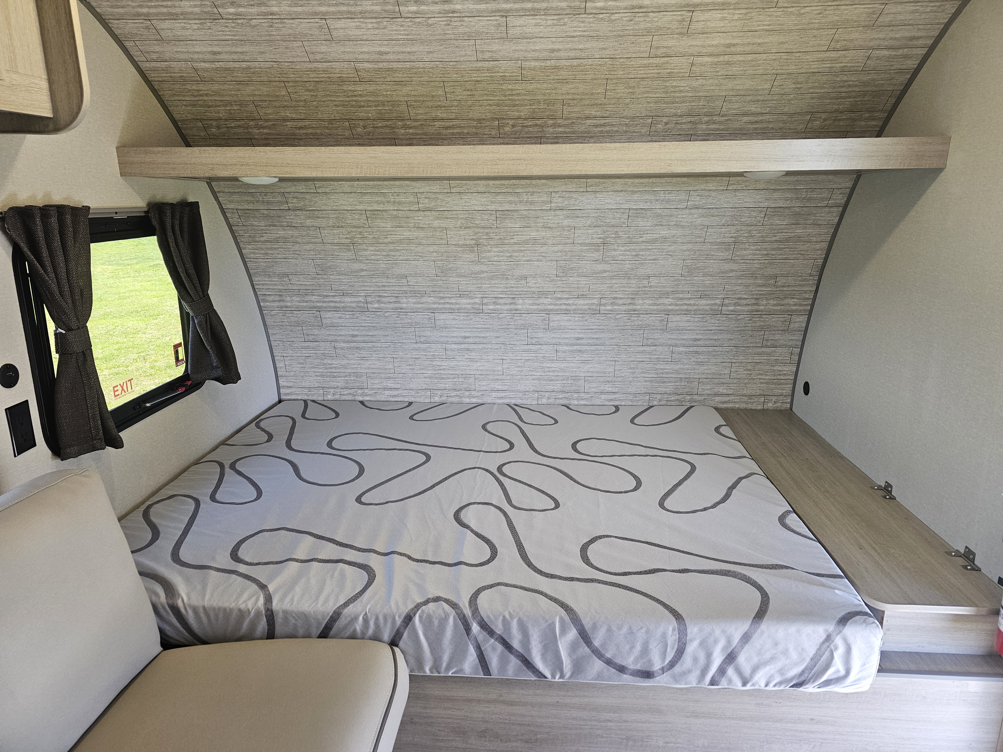 Inside an **RV rental**: a compact sleeping area with a patterned bed, wood-textured walls, and a window for comfortable travel.. Forest River Catalina 16BHX 2024