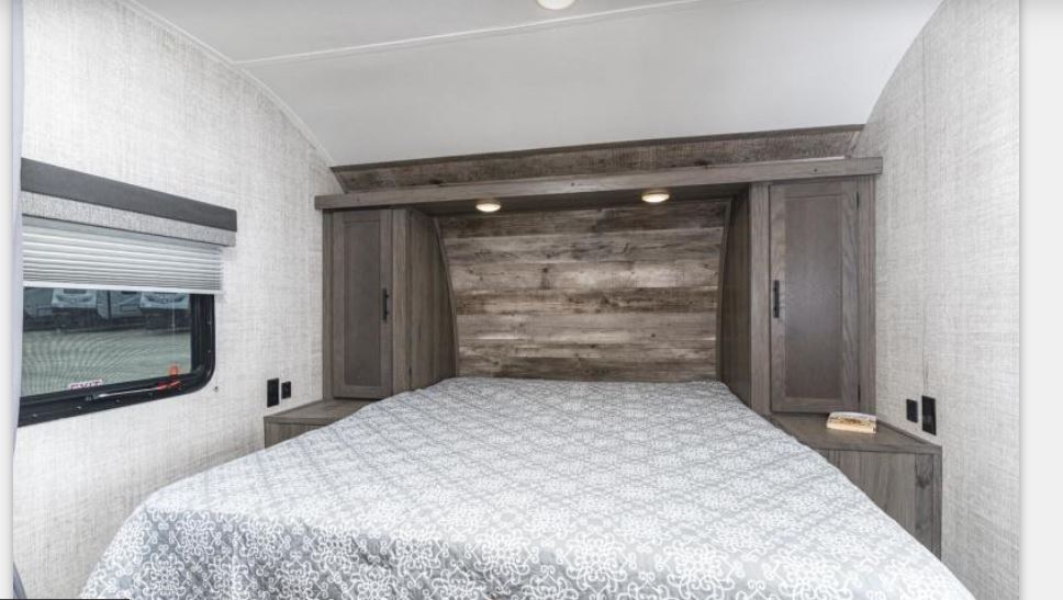 RV rental bedroom with bed, light patterned quilt, wooden headboard with lights, and storage cabinets.. Gulf Stream Kingsport 2022