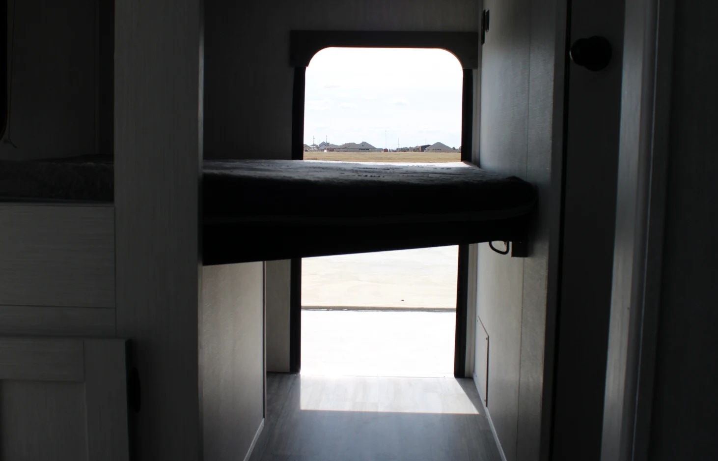 Inside an RV rental: view of bunk beds, an outdoor window scene, and an open rear ramp for easy access, typical of a toy hauler.. Forest River Coachmen Apex UtlraLite 284BHSS 2024