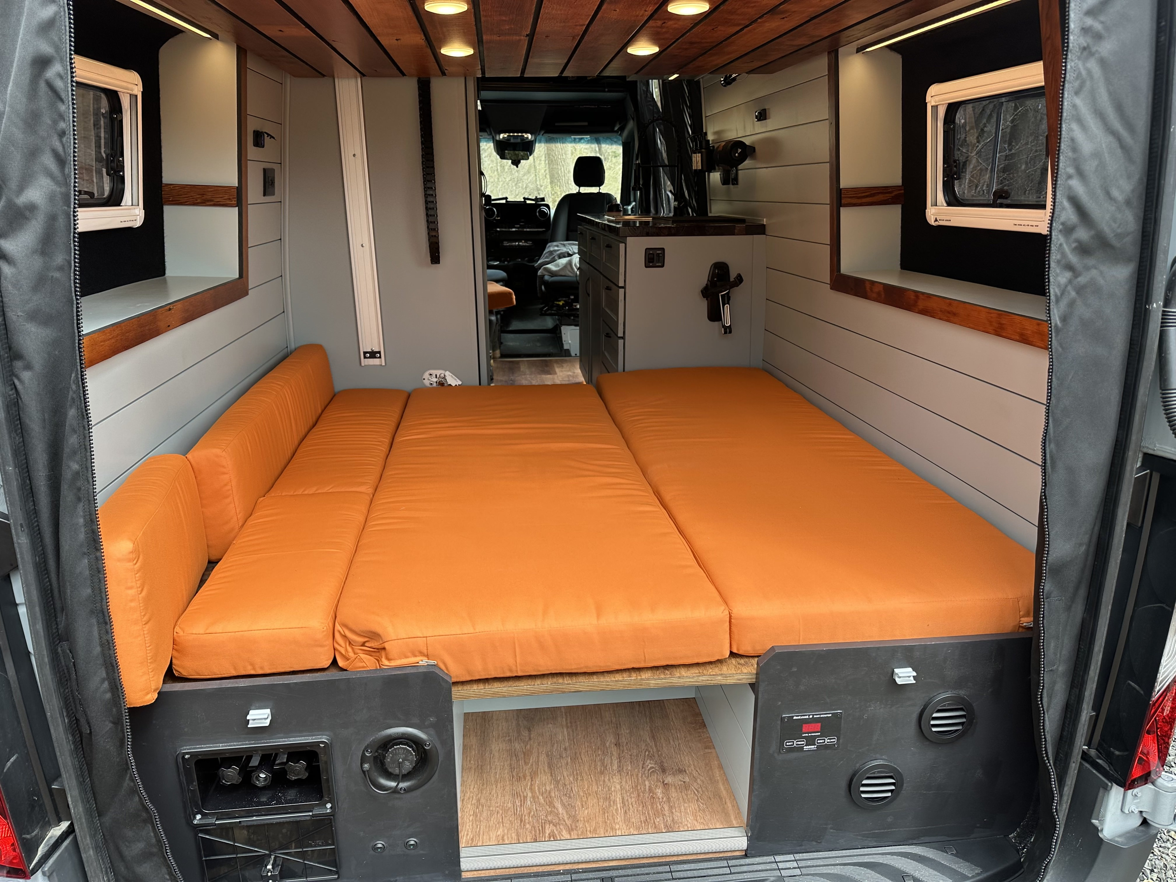 Bright RV rental camper van interior. Features a versatile orange cushioned bed/lounge, wood ceiling, and compact kitchenette.. Mercedes-Benz Sprinter 2023