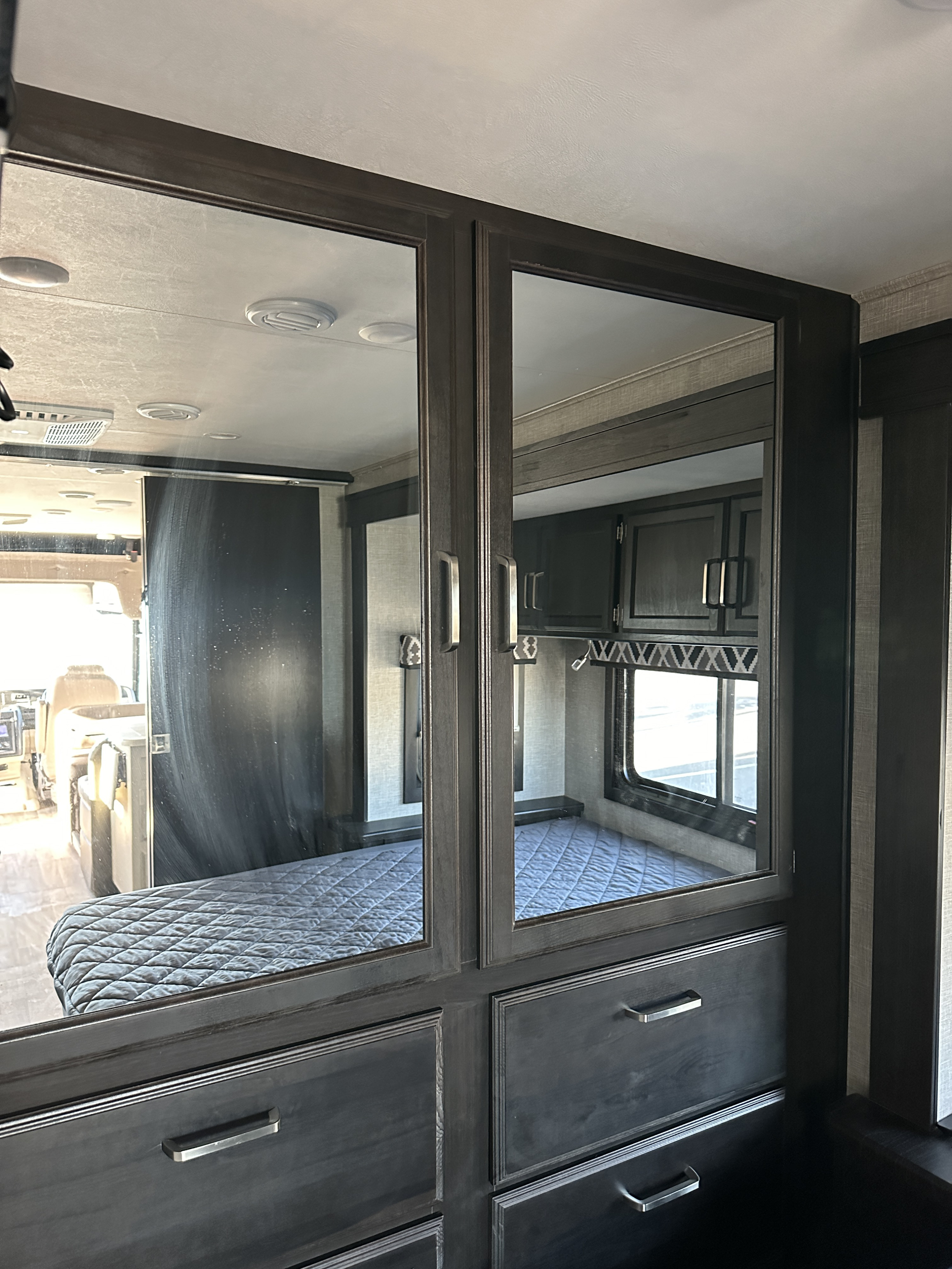 Inside an RV rental: Mirrored bedroom storage reflecting the bed, window, and front cabin area. Compact living for your travels.. Entegra Coach vission 27a 2022