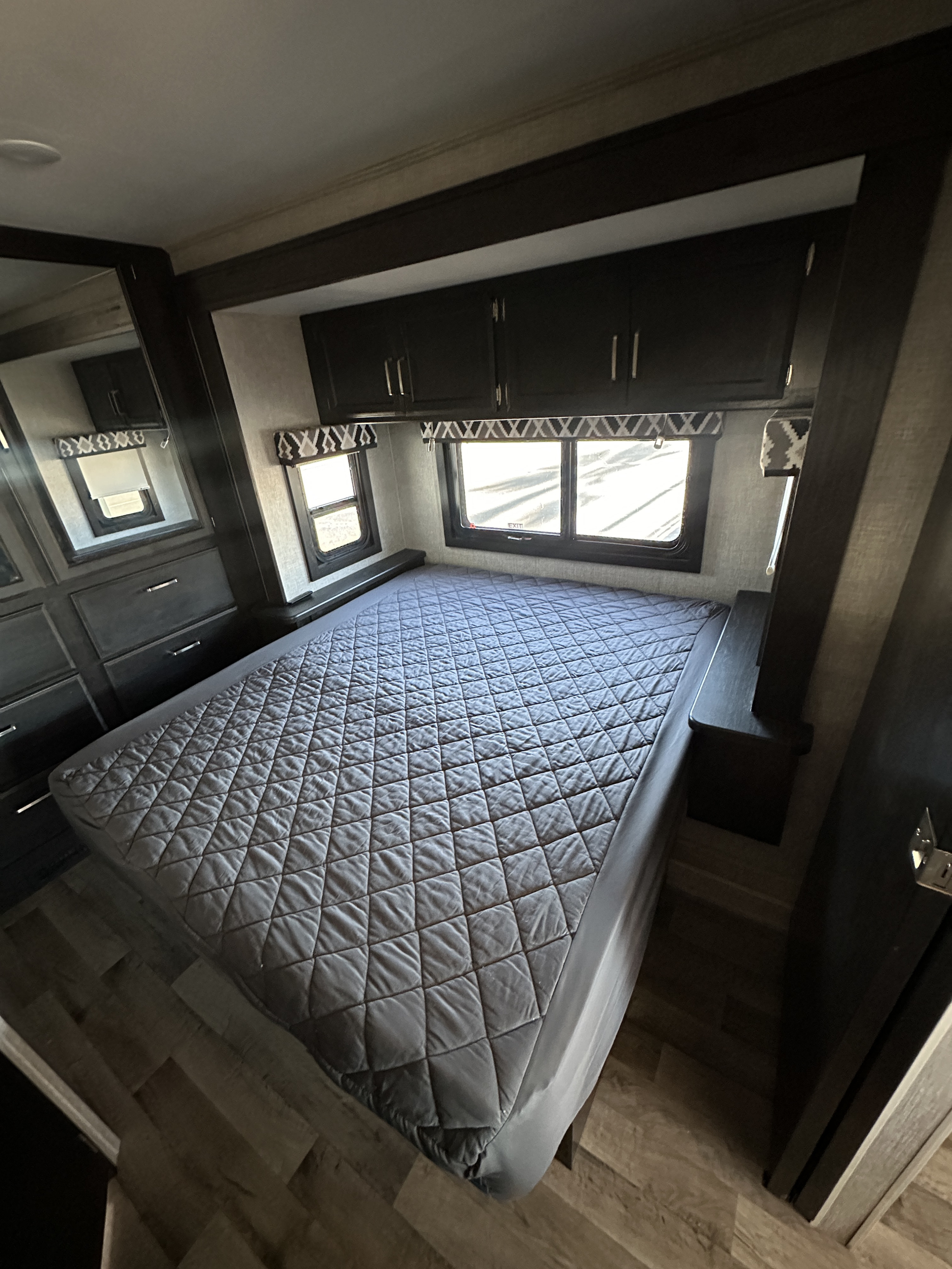 RV rental bedroom featuring a large bed with a gray quilted cover, overhead cabinets, and multiple windows. Cozy travel space.. Entegra Coach vission 27a 2022