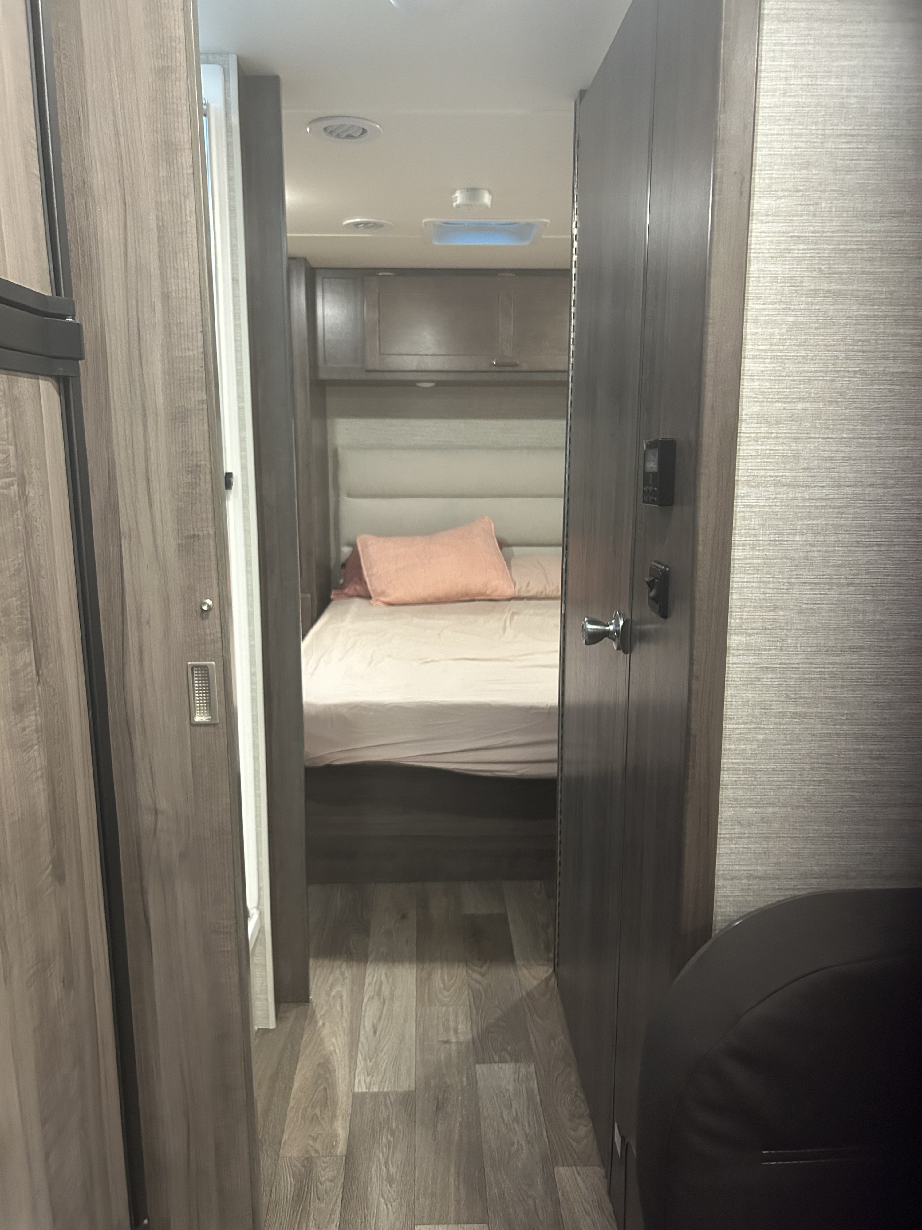 RV rental interior. A cozy bedroom with a comfortable bed and overhead storage is seen through a narrow hallway.. Winnebago Minnie Winnie 2023