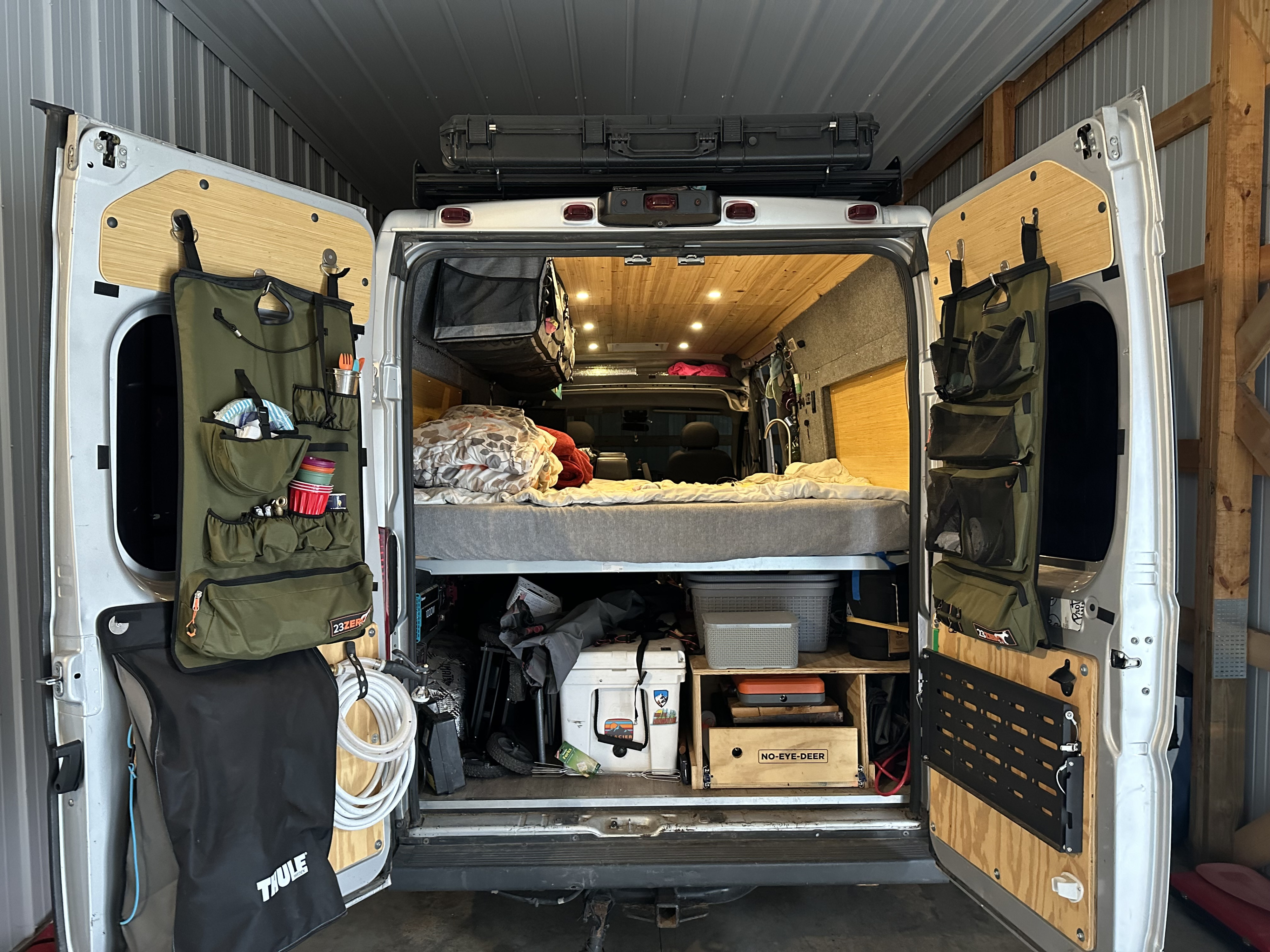 RV rental camper van interior from rear: features a raised bed, organized storage, and door-mounted custom panels.. Dodge Promaster 2014