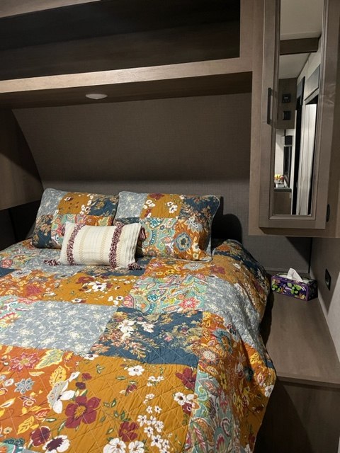 Cozy RV rental bedroom with a vibrant patchwork quilt, pillows, and built-in overhead storage.. Highland Ridge RV Open Range 2023